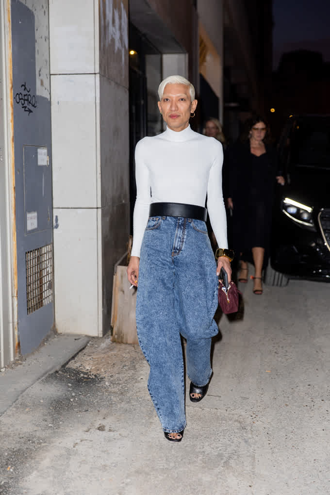 Frau spaziert auf Gehweg, trägt weißes Longsleeve in Kombination mit Statement-Gürtel und Denim-Hose