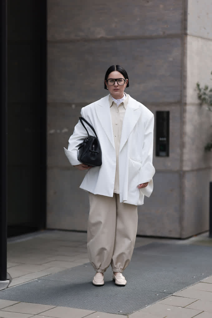 Frau trägt weißen Oversize Blazer, kombiniert mit beigen Barrel Pants und schwarzer Handtasche