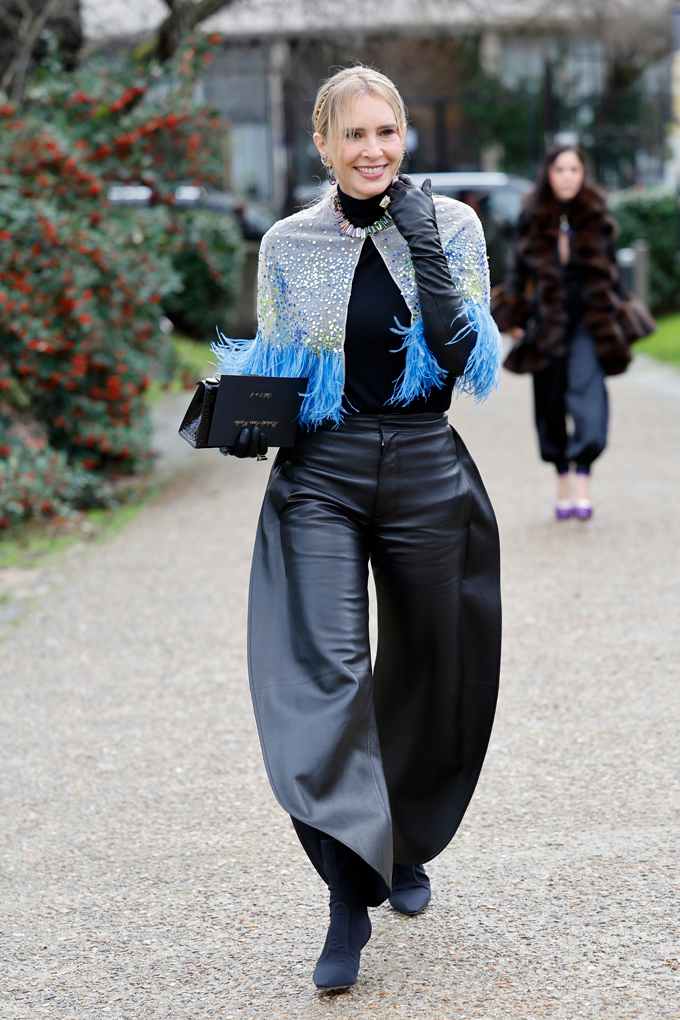 Lächelnde Dame, gekleidet in schwarzen Rolli mit Cap-Jacke und weit ausfallender Barrel Hose in Lila