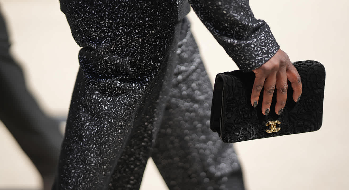 Person mit schillerndem Jacquard-Outfit spaziert, trägt eine passende Chanel-Tasche in der Hand