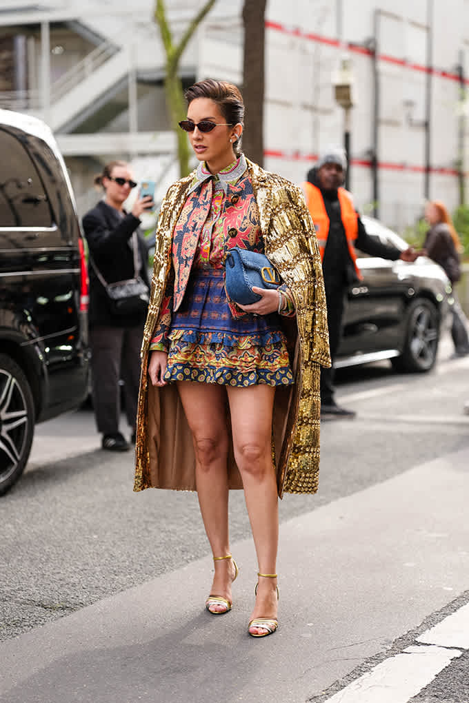 Frau auf Straße trägt goldenen Jacquard-Mantel als Glam-Layer über einem farbintensiven, gemusterten Mini-Dress