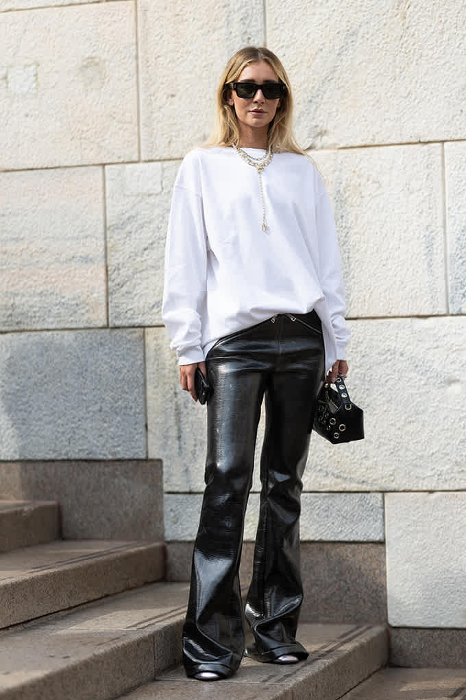 Blonde Frau auf Treppenstufe, trägt weißen OVersize-Pullover mit schwarzer Lederhose