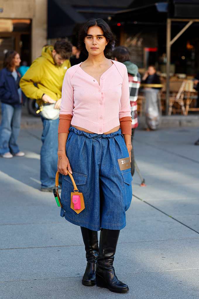 Frau steht auf Straße, trägt rosa Top, kombiniert mit blauer Culotte und schwarzen Stiefeln