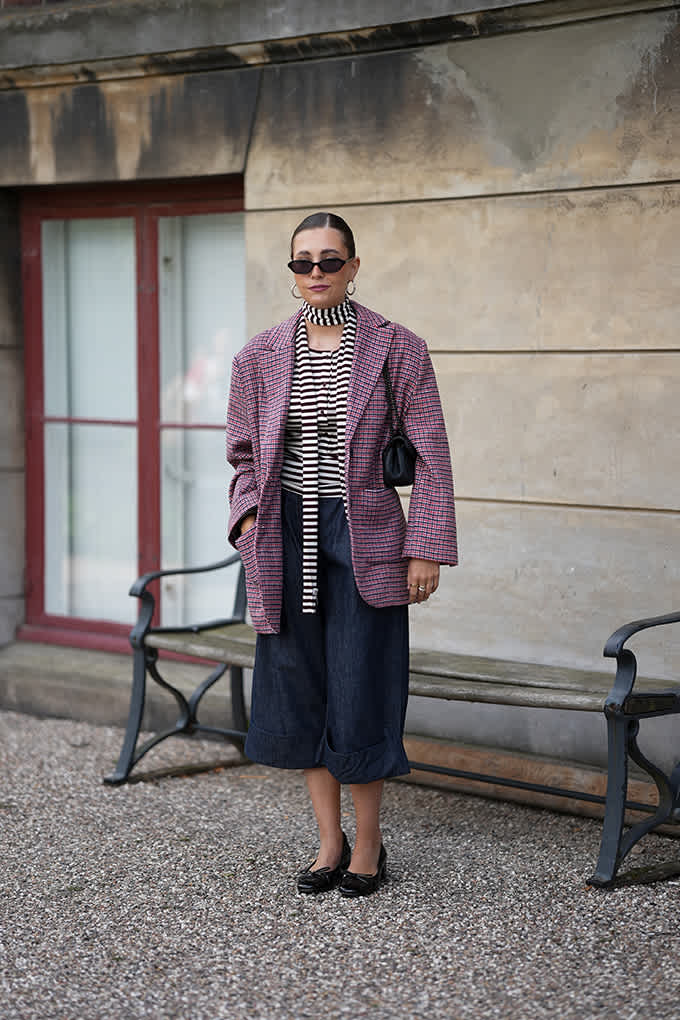 Frau vor Sitzbank, trägt magentafarbene Jacke zu Streifen-Top und schwarzer Culotte
