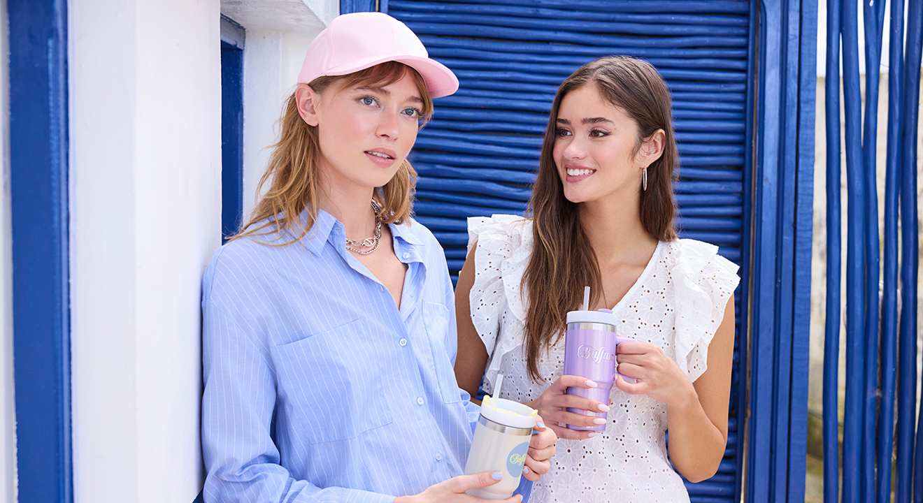 Zwei Frauen in luftigen Sommer-Outfits stehen mit Getränken nebeneinander