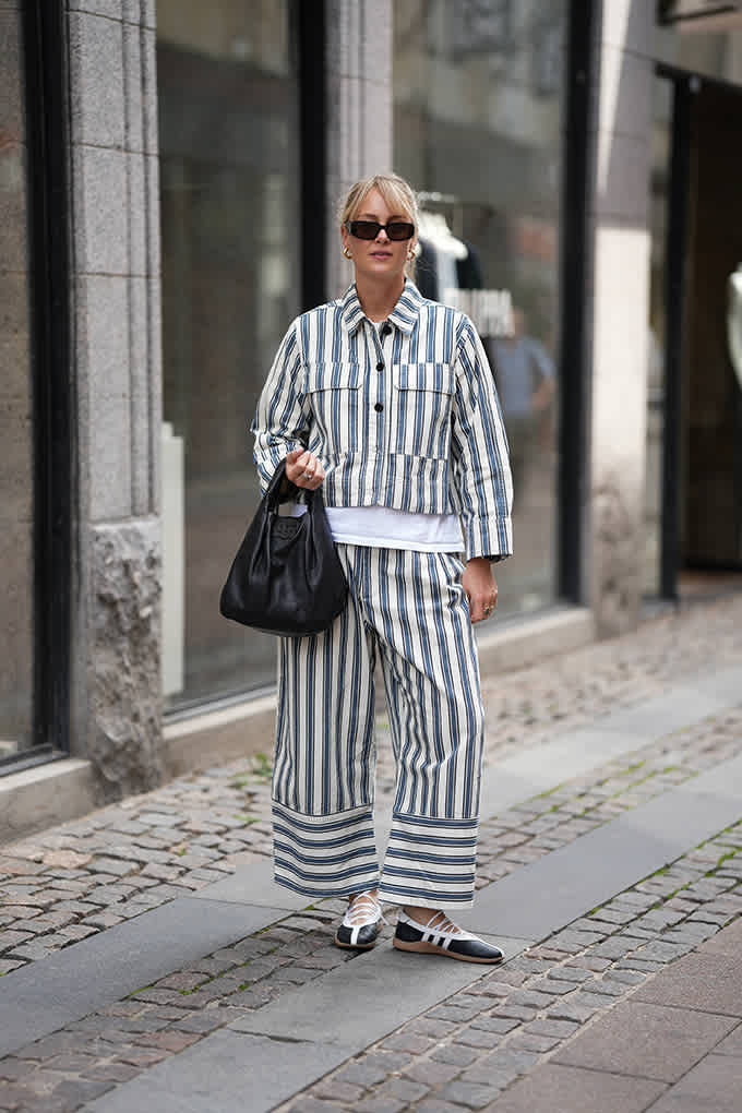 Frau trägt auffälliges Streifen-Outfit in urbaner Kulisse, kombiniert mit Sneakerinas und Handtasche