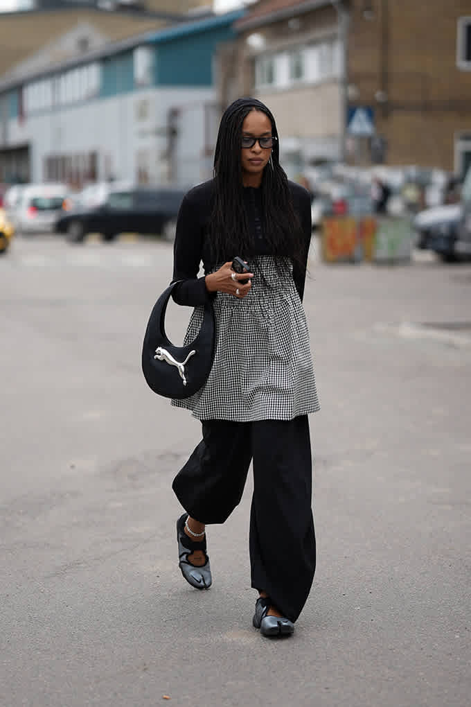 Frau in schwarz-grauem Kleid, kombiniert mit Palazzohose, Sneakerinas und Baguette Bag