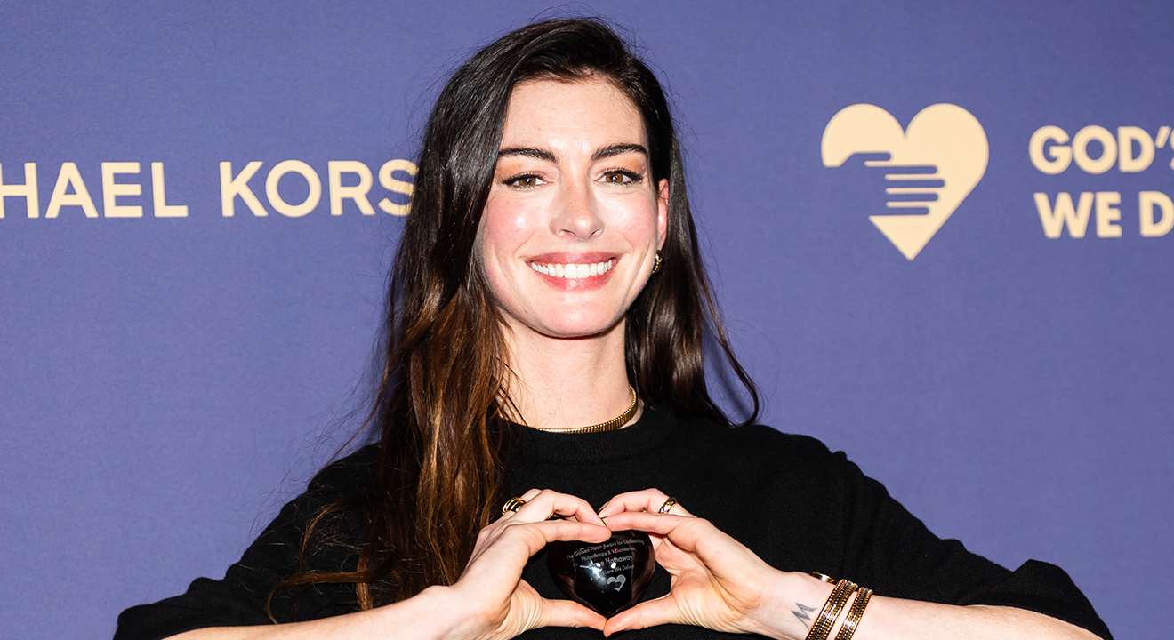 Anne Hathaway steht vor Logo-Wall, formt Herz mit den Händen
