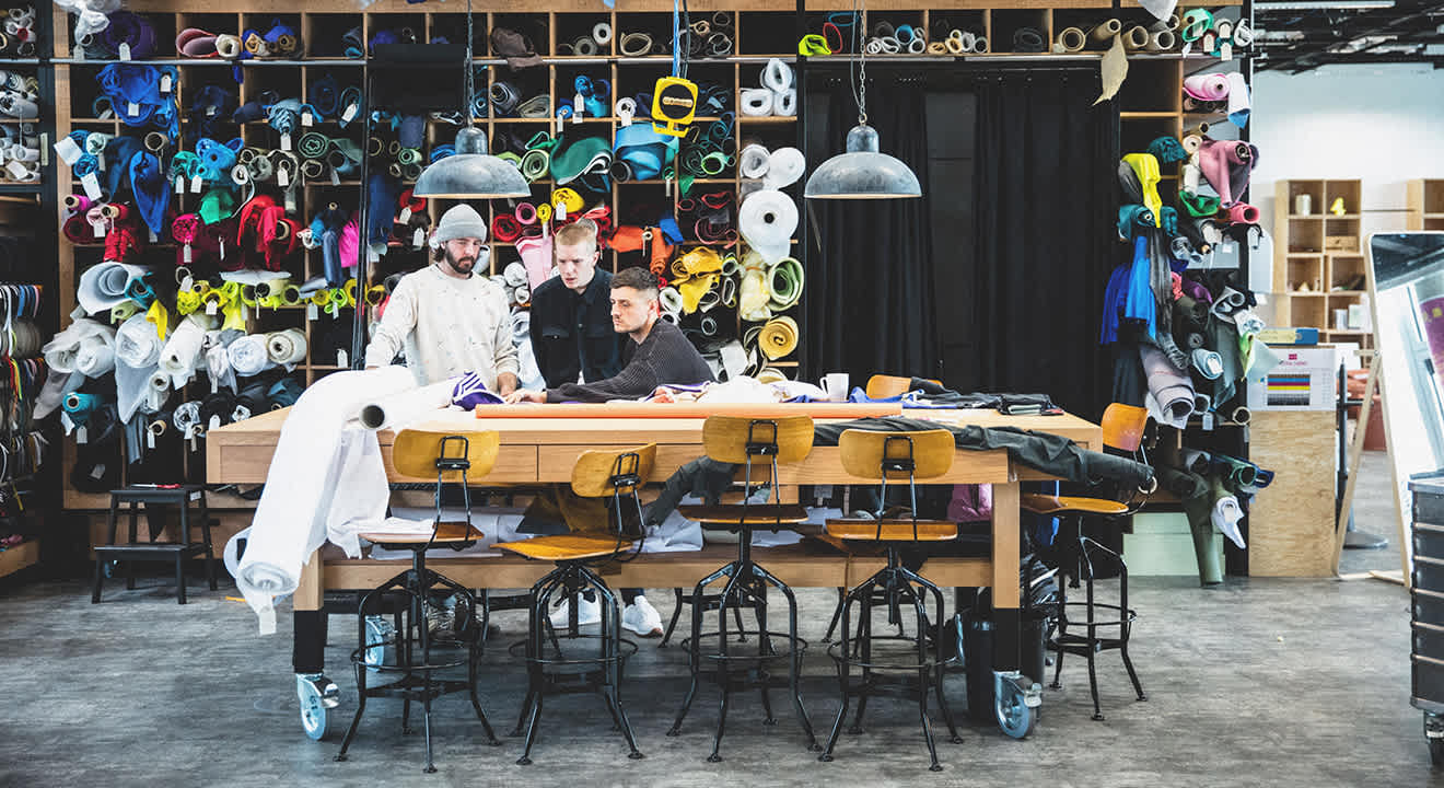 Drei Männer arbeiten in einer Schuhmacherei an einem Arbeitstisch