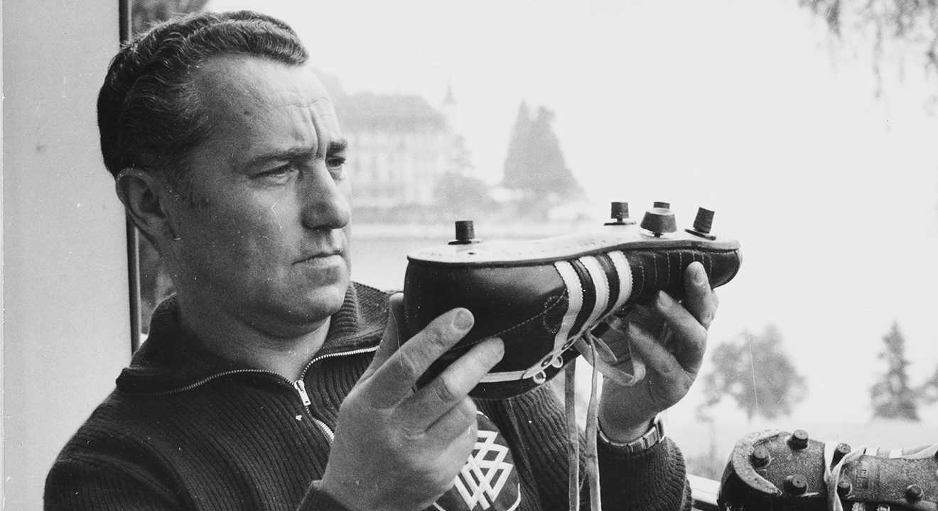 Adolf Dassler betrachtet einen adidas-Fußballschuh