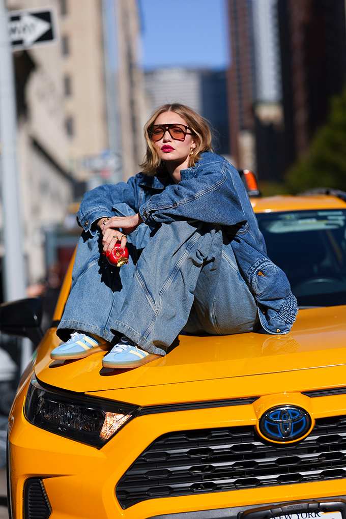Frau in Denim-Outfit sitzt auf Motorhaube eines gelben Sportwagens