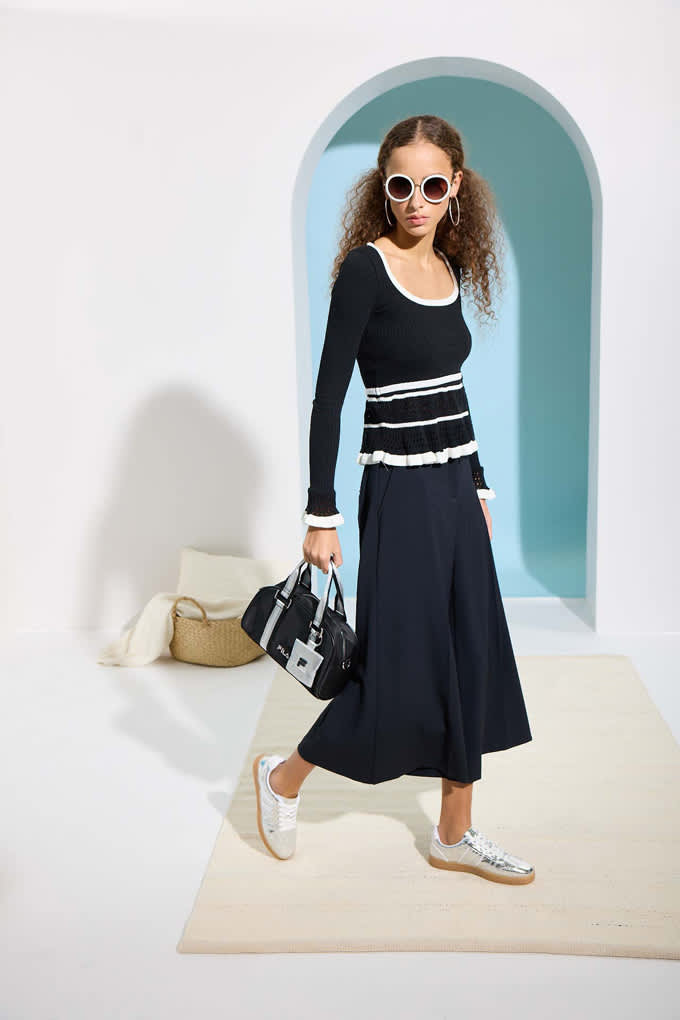 Frau trägt schwarzes Strick-Kleid, kombiniert mit Handtasche und Sneakern