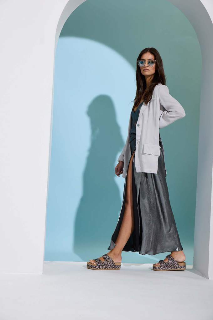 Frau in Steinbogen trägt weißen Blazer über silbernem Mirror-Piece-Kleid