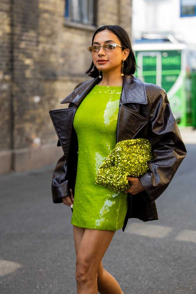 Frau trägt schwarze Lederjacke über grün-glitzerndem Kleid, mit glitzernder Tasche