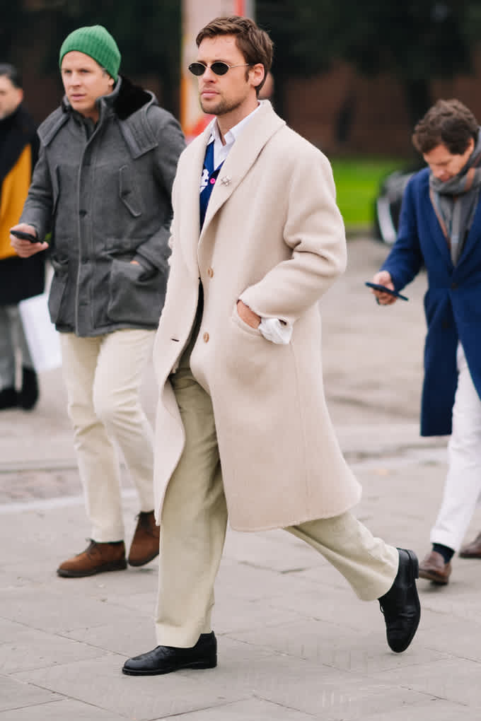 Mann in beigem Mantel und heller Cordhose im Layering-Look