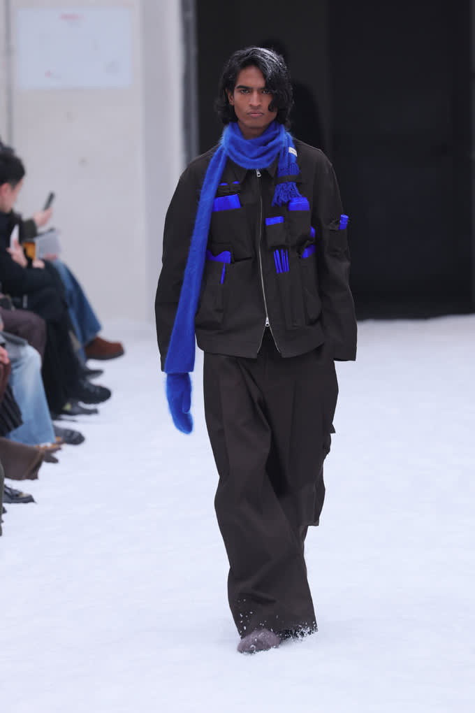 Schwarzhaariger Mann mit blauem Schal, kombiniert mit schwarzer Utility-Jacke und -Hose