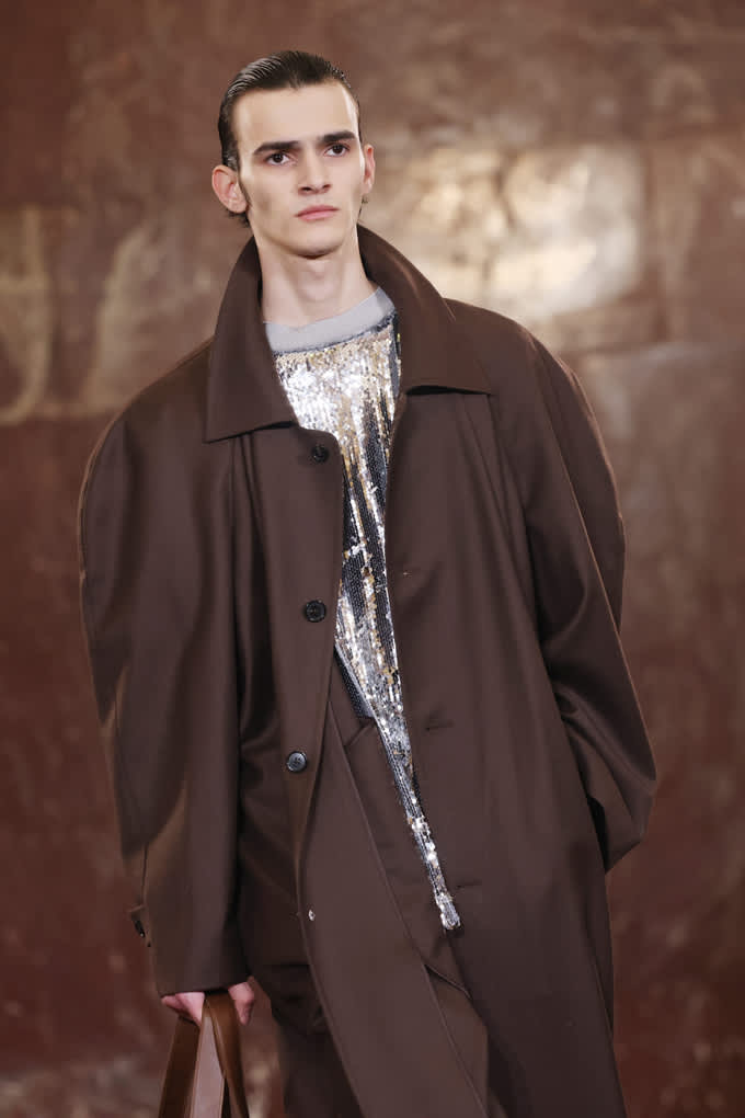 Männliches Model auf der Pitti Uomo 2026, trägt braunen Mantel mit schimmerndem Pailetten-Top