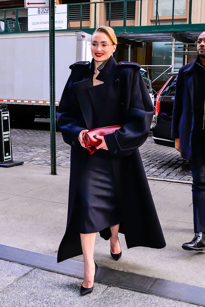 Sophie Turner spaziert auf Straße, trägt Oversize Mantel mit tiefroter Clutch