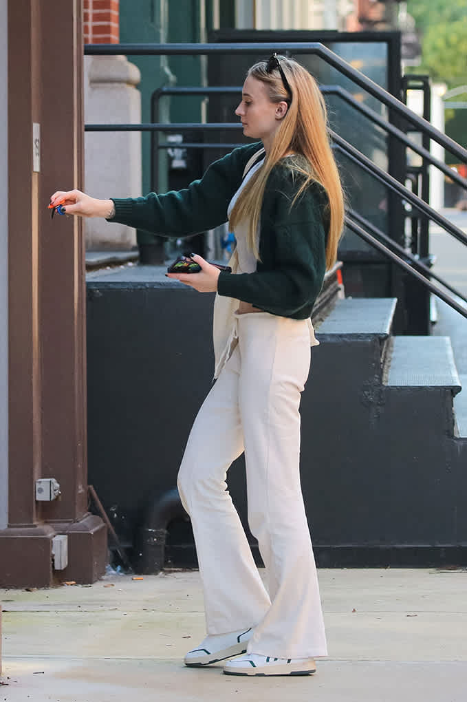 Schauspielerin Sophie Turner in dunkelgrünem Blazer, mit cremefarbener Schlaghose, auf dem Gehweg