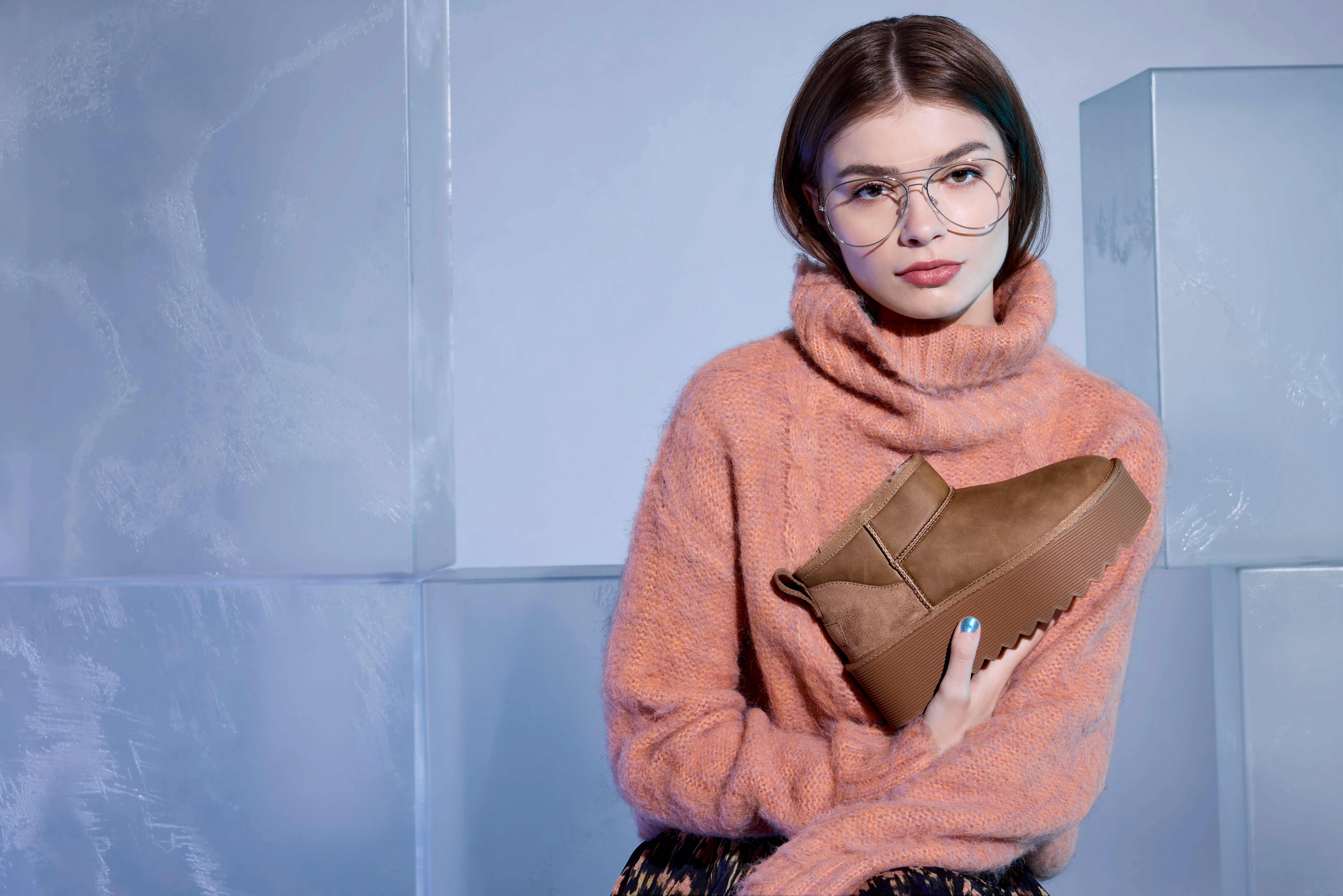 Frau mit Brille und rosa Pulli hält braunen Snowboot lässig vor der Brust