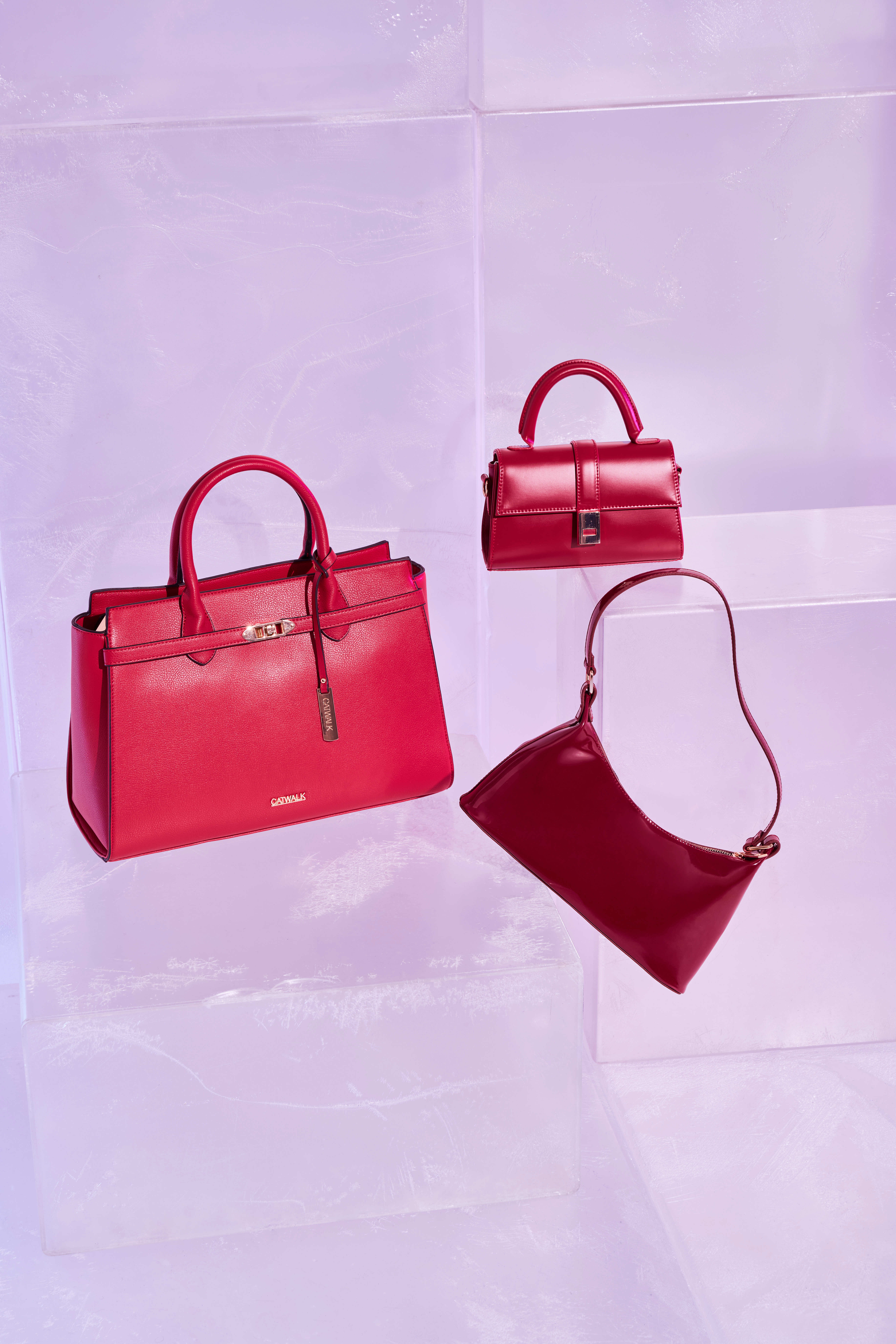 Drei tiefrote Handtaschen, auf transparenten Podesten stehend, vor Studio-Hintergrund