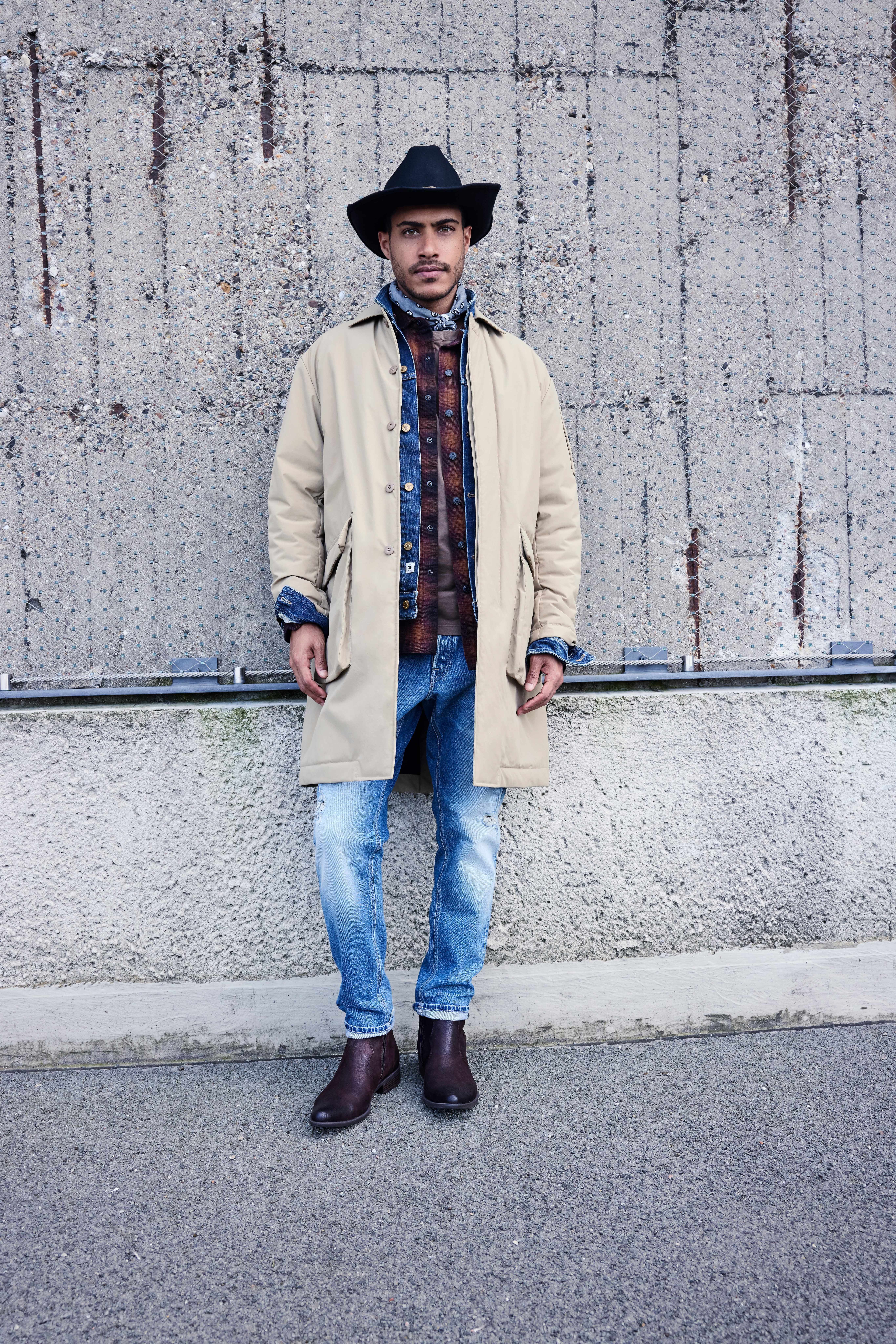 Mann steht vor grauer Wand, gekleidet in Cowboy-Outfit mit Cowboy Boots