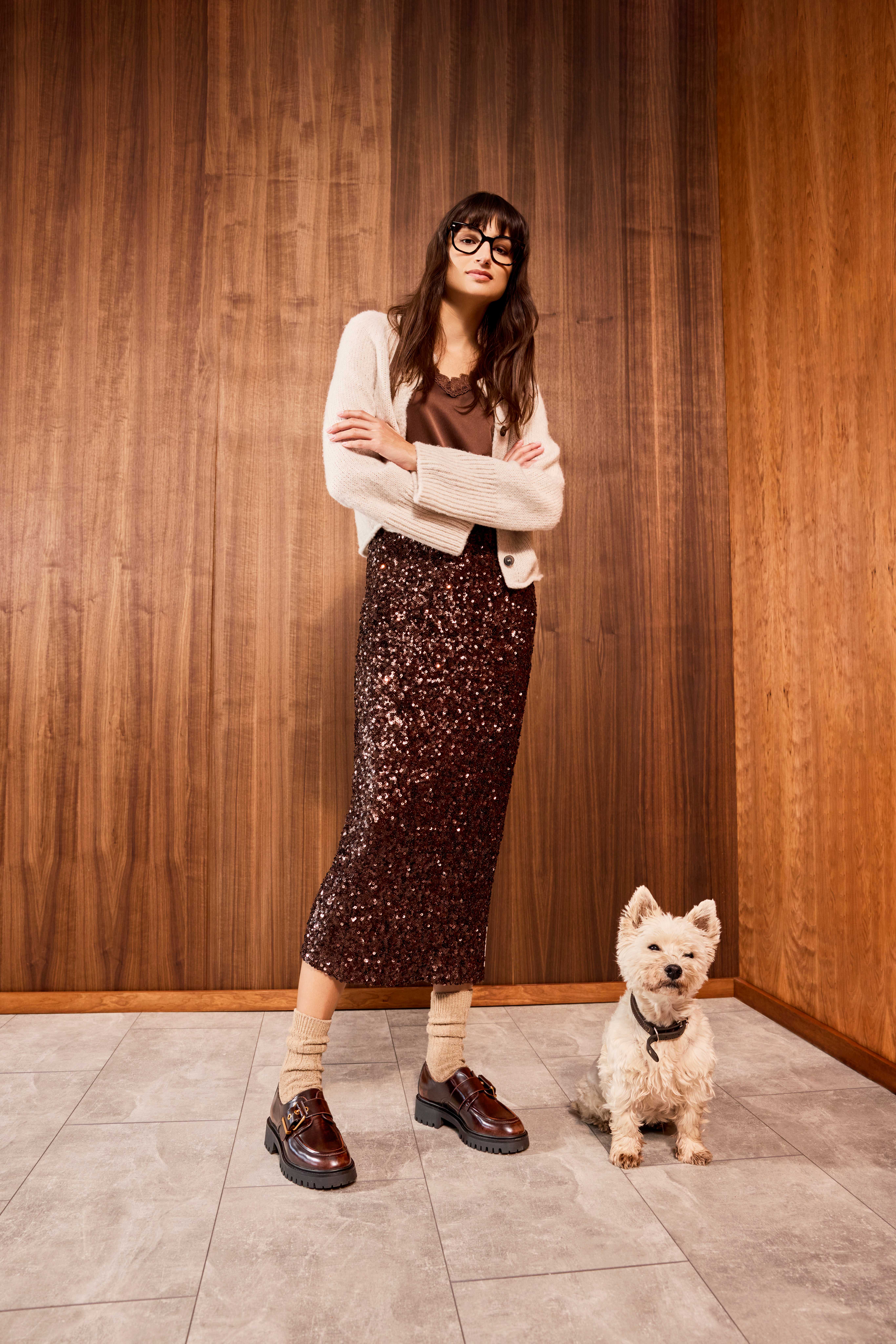 Frau mit chunky Loafern steht in Animalprint-Outfit neben kleinem Hund