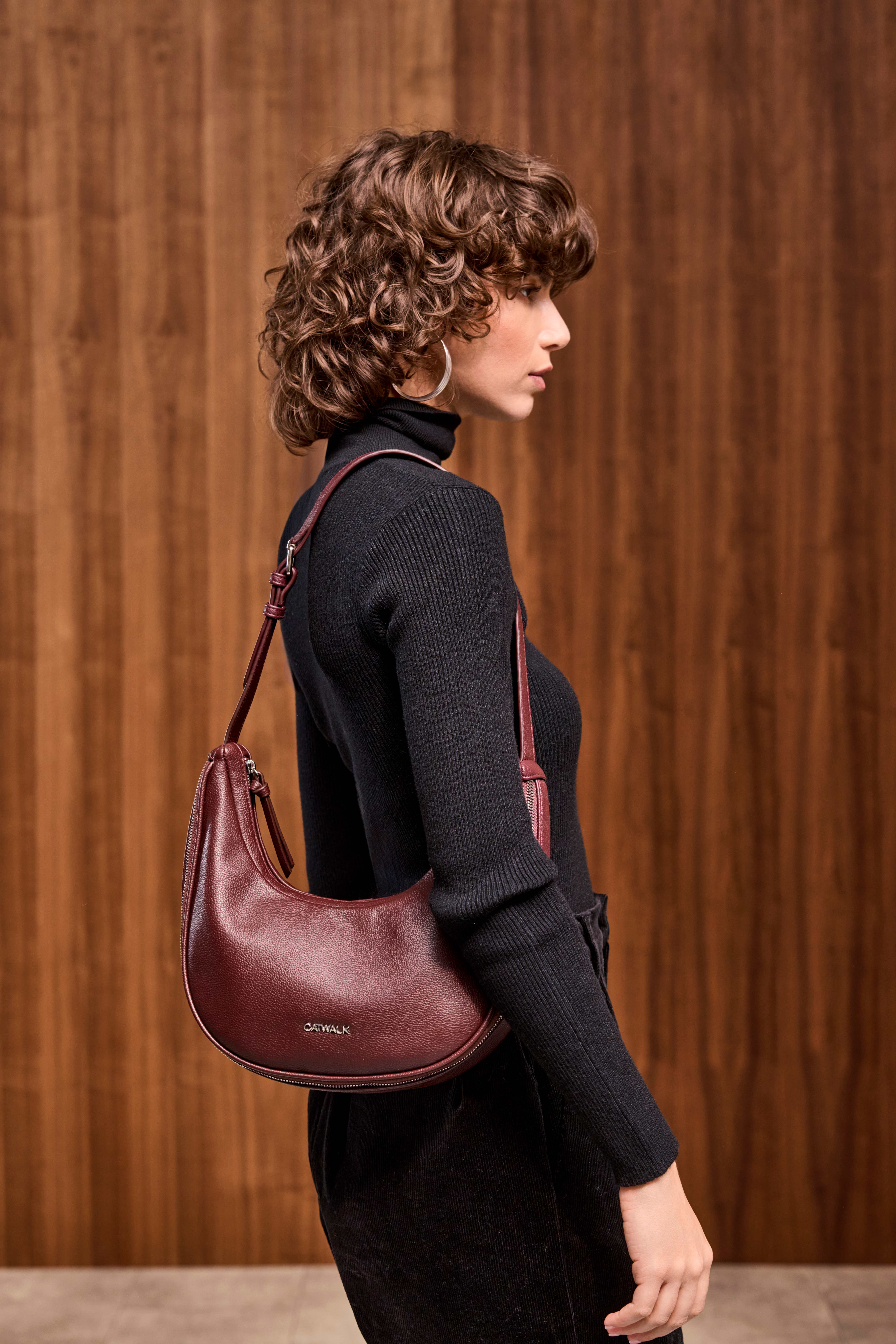 Frau in schwarzem Strickkleid, trägt violette Halfmoon Bag um die Schulter
