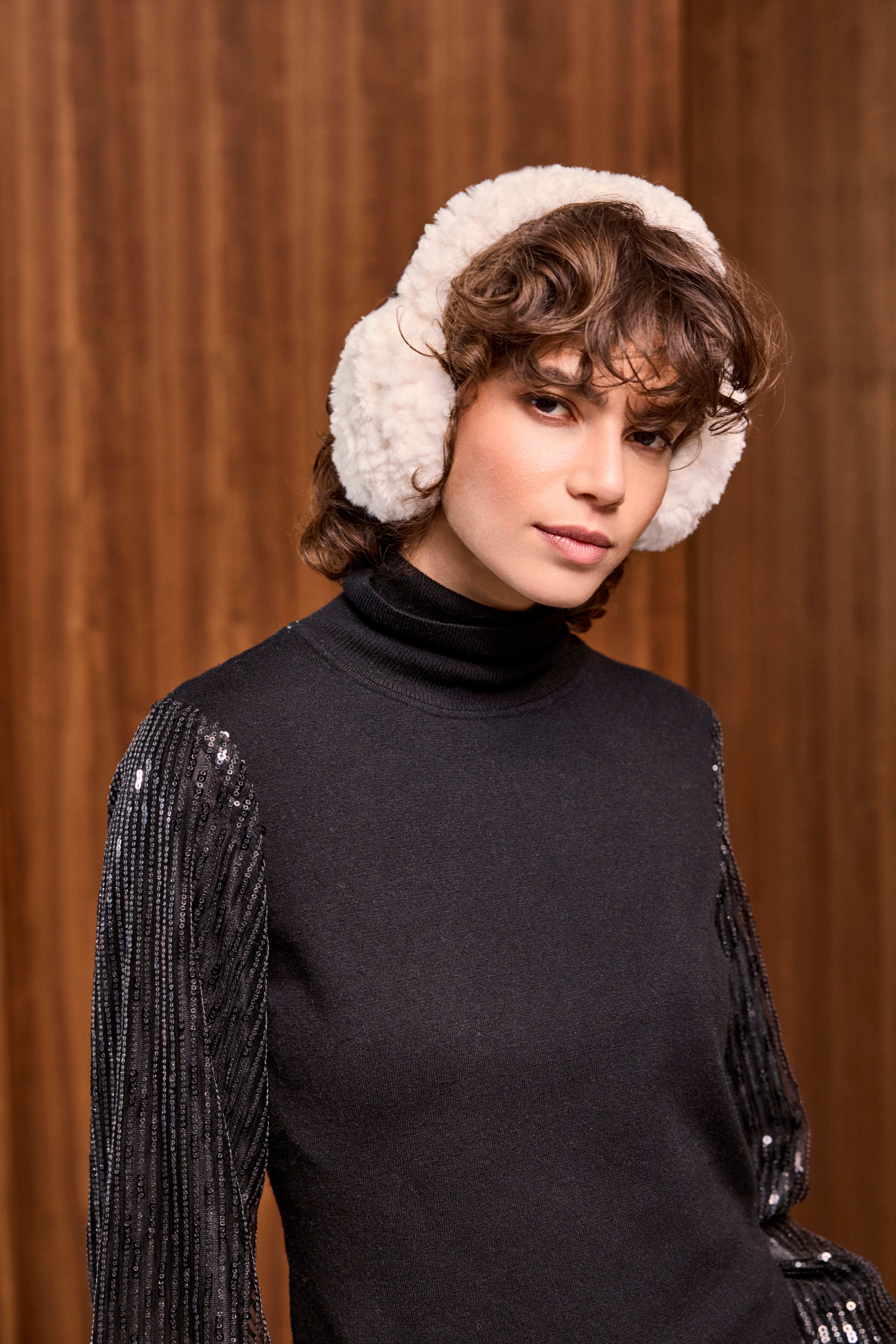 Brunette Fra, gekleidet in schwarzen Wollpullover, mit flauschigen Ohrenwärmern in Pink