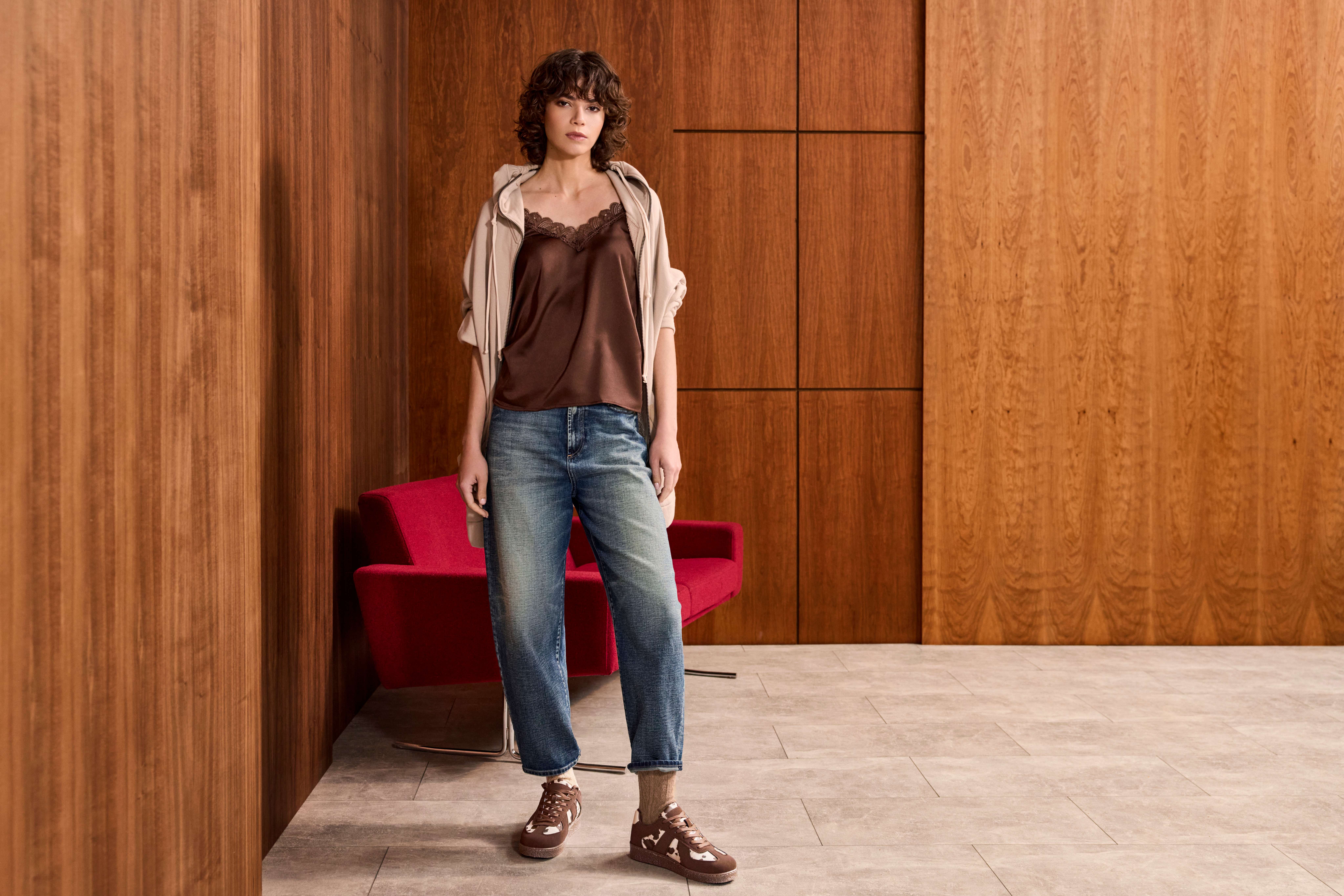 Frau in engen Jeans steht lässig vor roter Couch 