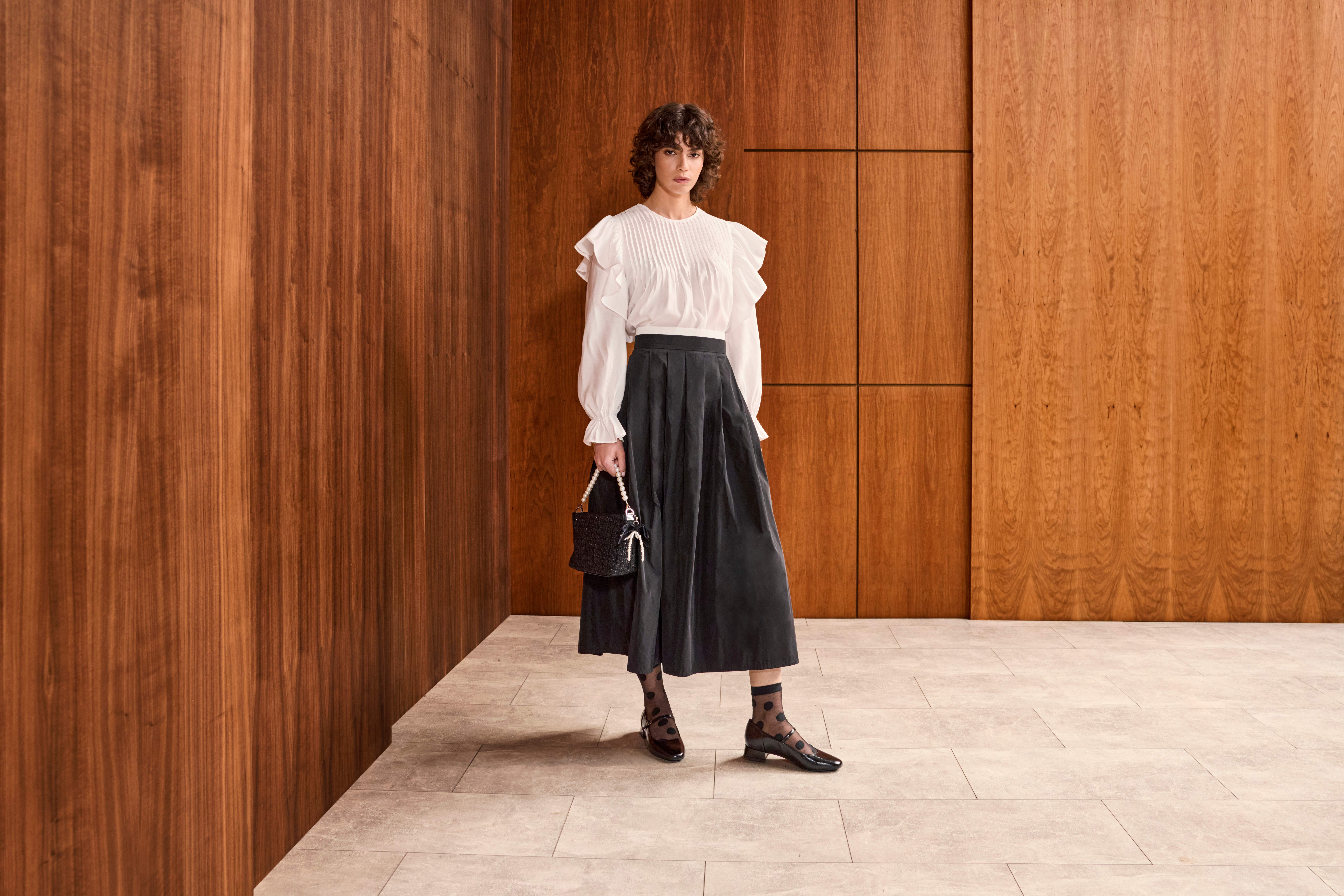 Frau in cleanem Look mit weißem Langarm-Top, langem Rock und schwarzer Handtasche