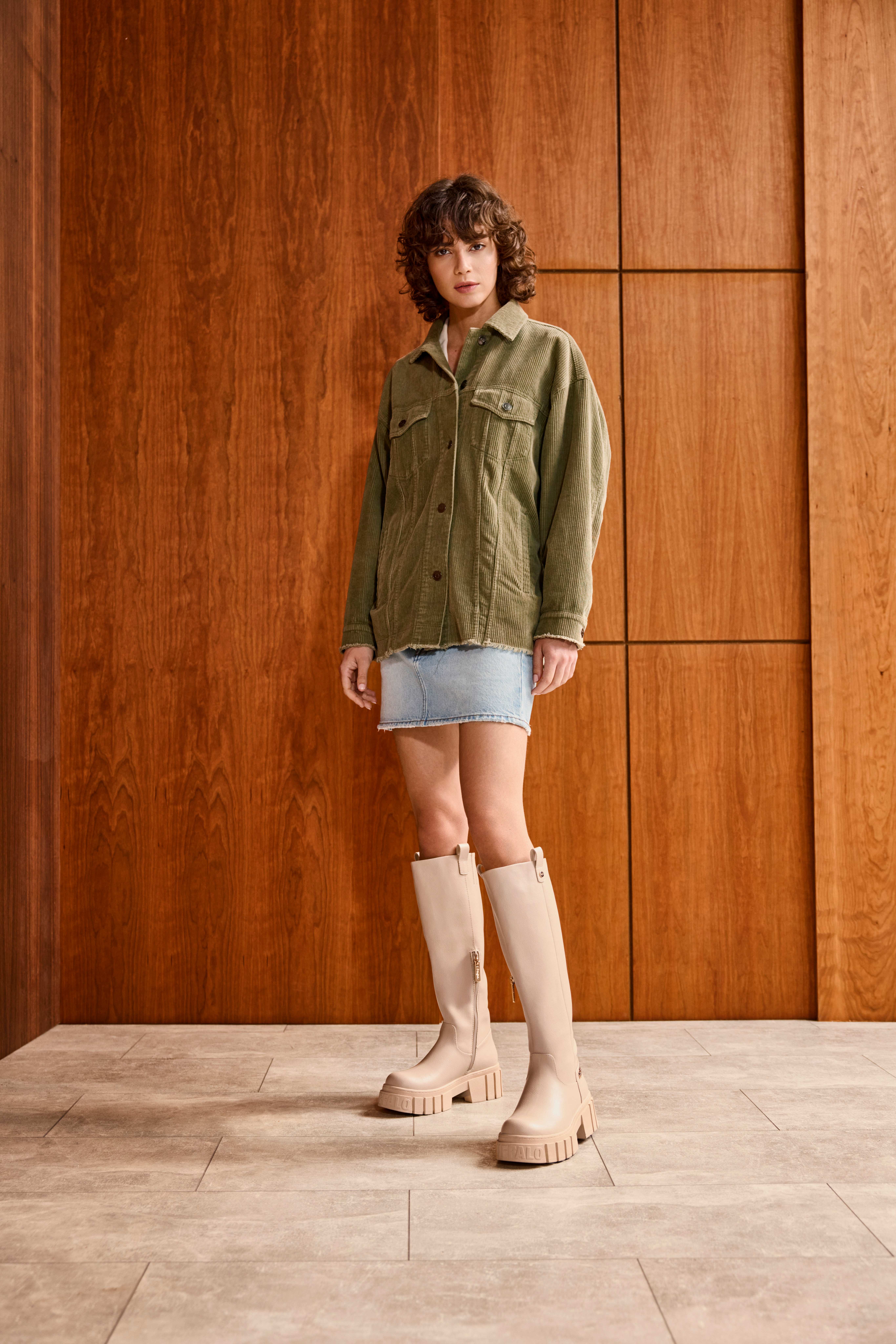 Frau in grünem Shacket, kombiniert mit Jeansrock, trägt dazu sandfarbene Gummistiefel