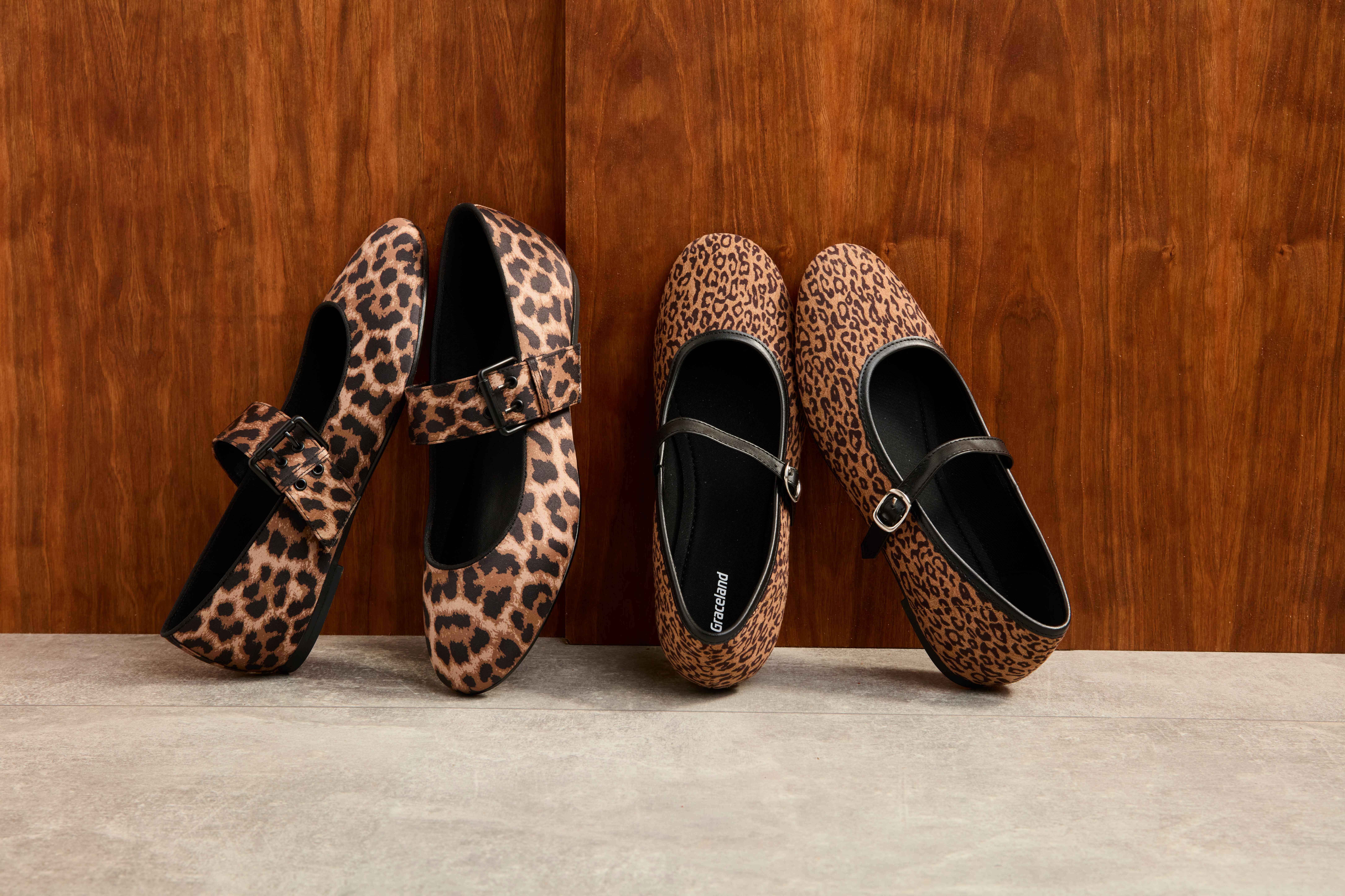 Zwei Stoff-Ballerinas in Animalprint-Optik stehen lehnend an Wand
