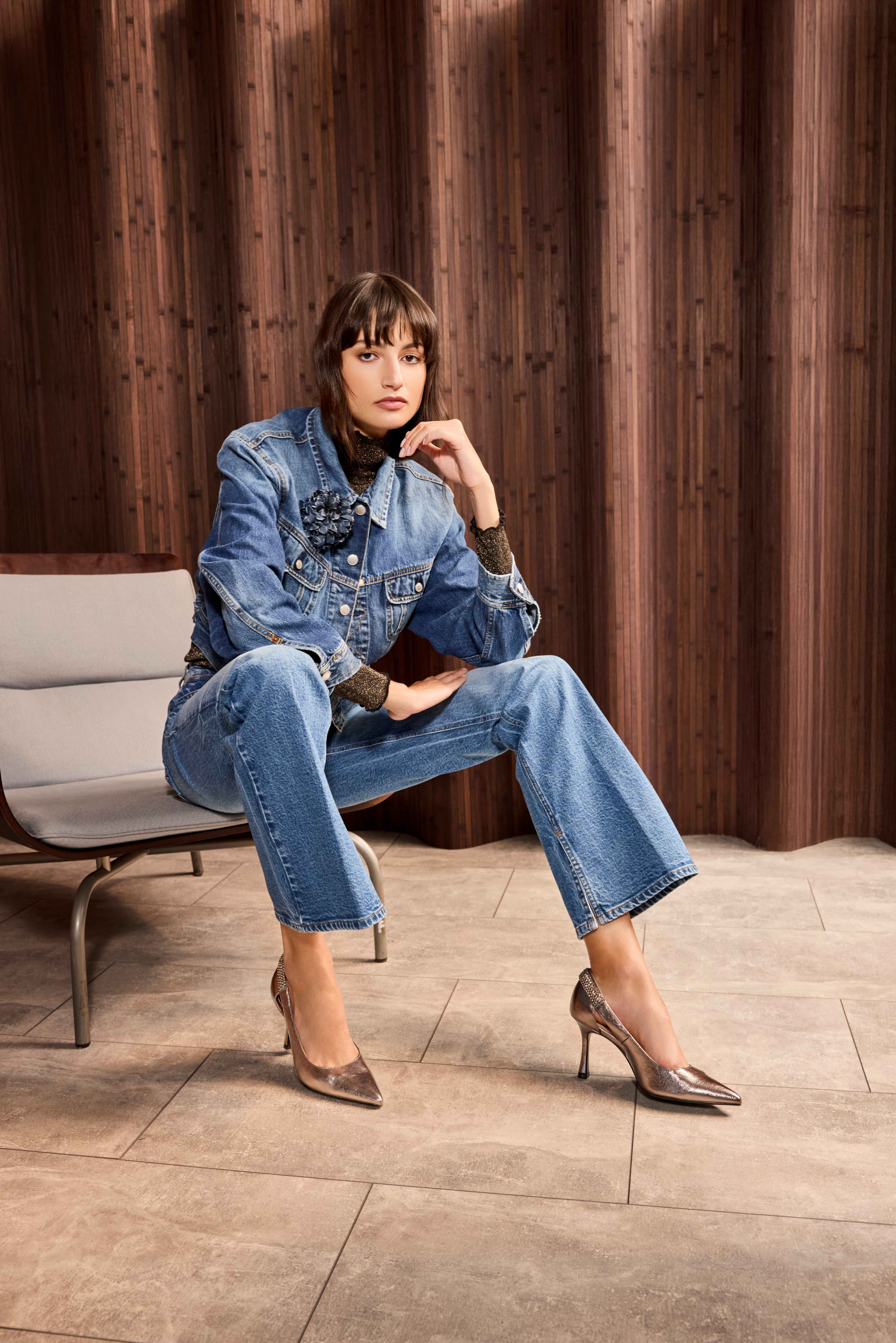 Frau trägt Jeansjacke und Jeanshose, mit silbernen Heels, sitzend auf Sofa