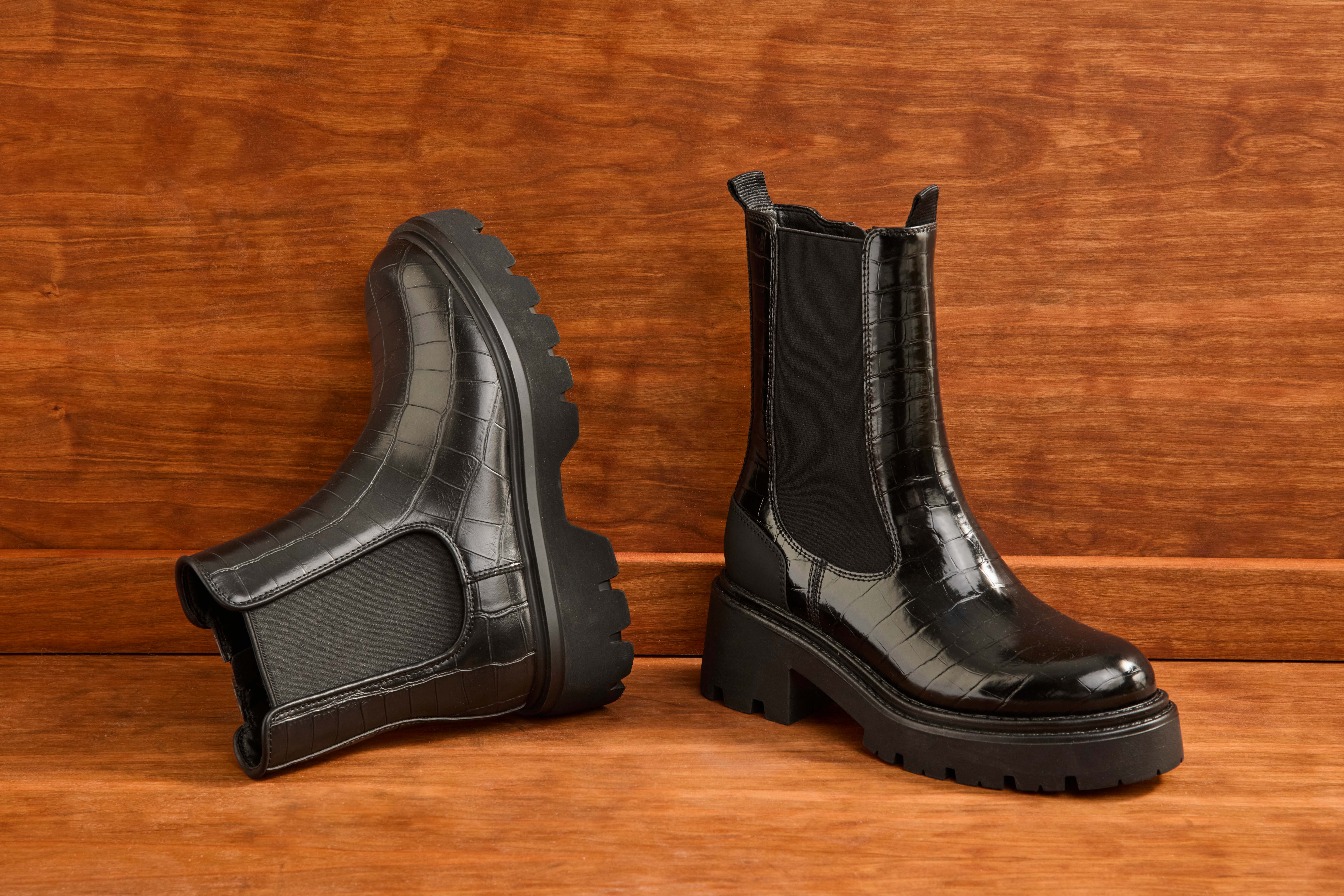 Zwei schwarze Stiefel aus Leder liegen vor Holzpaneel