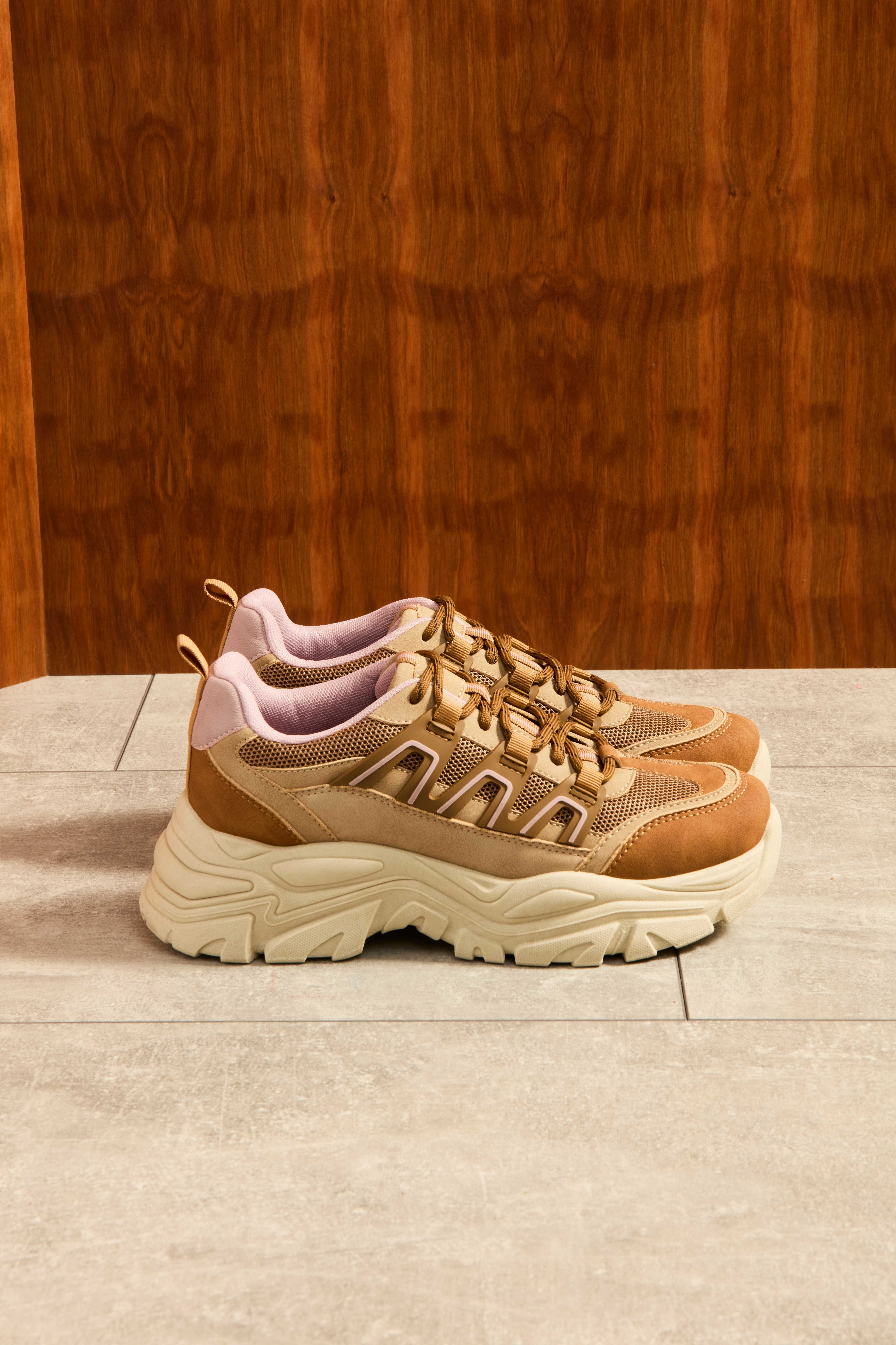 Ein Paar brauner Stoff-Sneaker mit dicker weißer Sohle auf Fliesenboden