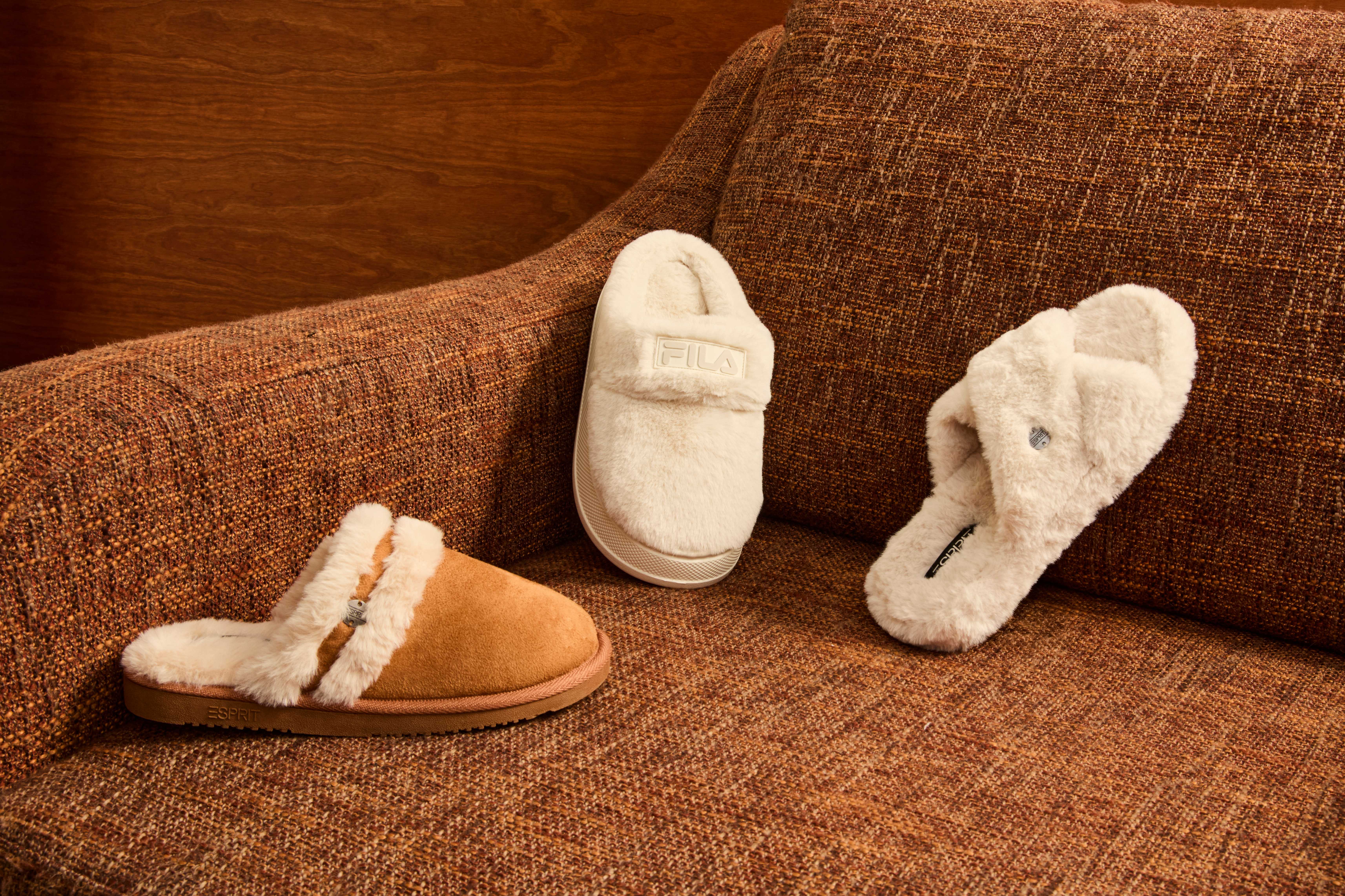 Drei kuschelige Slipper stehen auf einer braunen Couch 
