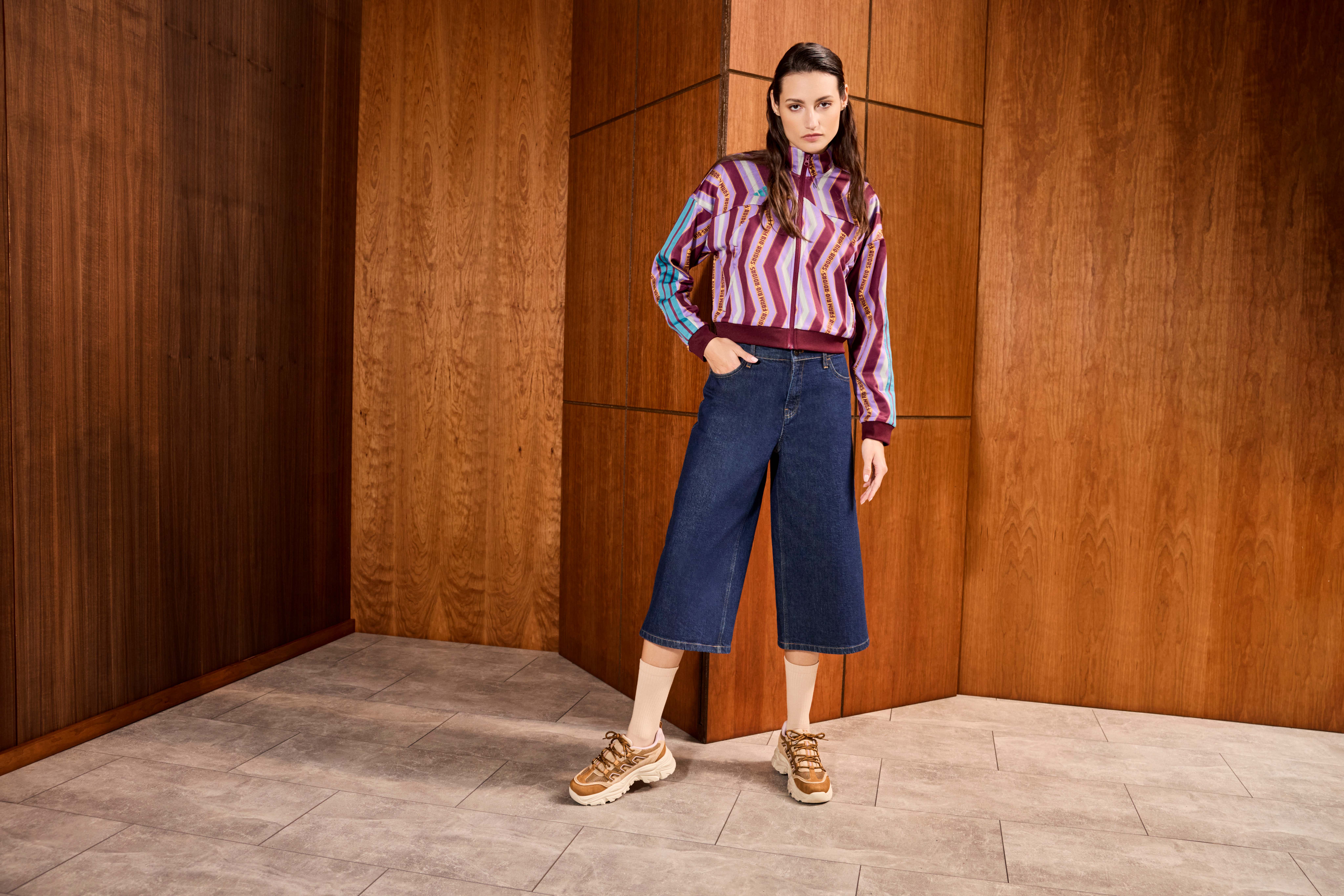 Frau steht in Raum, trägt gestreifte Bluse und weite Jeans-Hose, kombiniert mit braunen Sneakern