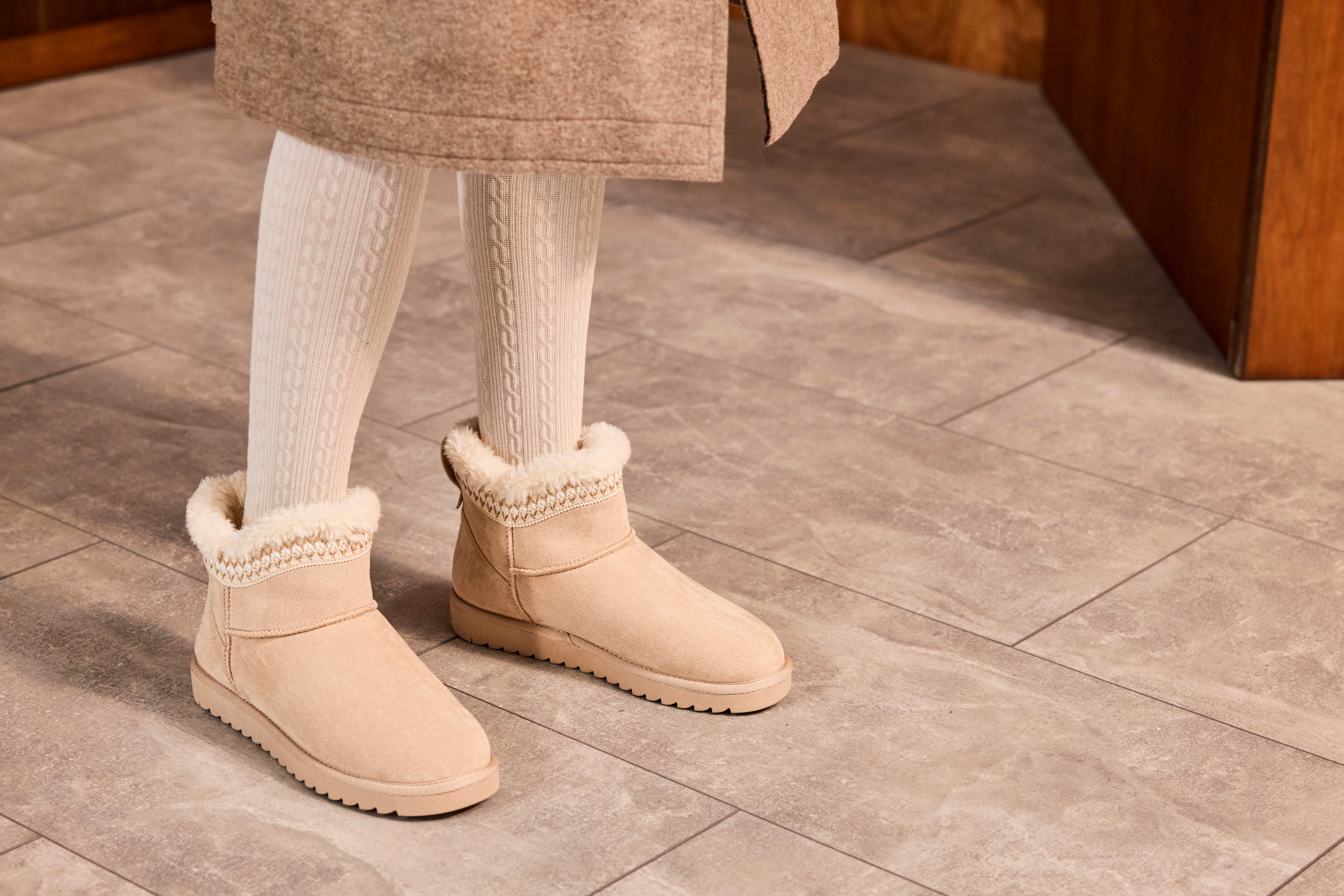 Frau steht in flauschigen Boots und langen Wollsocken auf gefliestem Boden