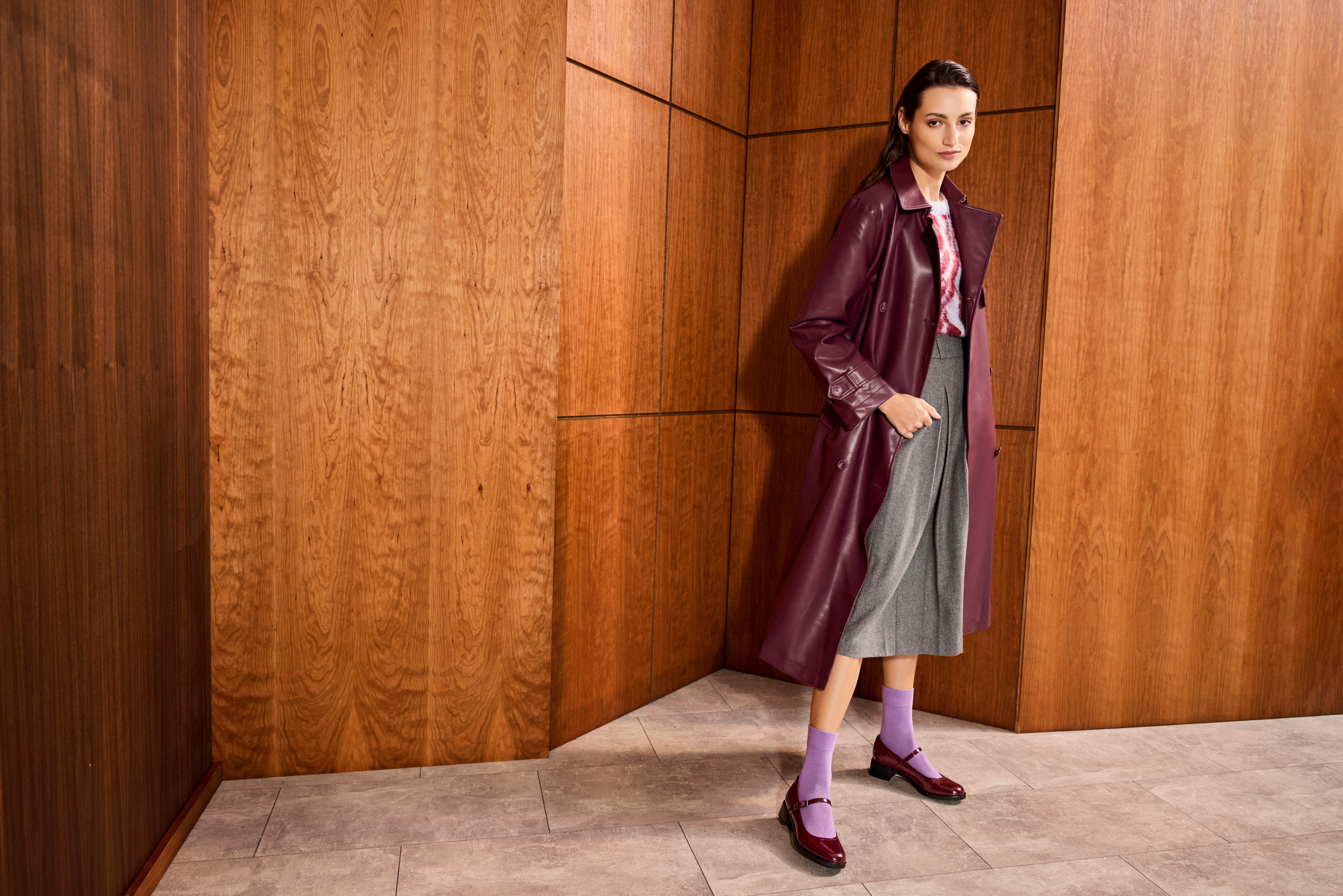 Frau in burgunderrotem Matrix-Mantel und grauem Kleid, trägt violette Socken zu Pumps