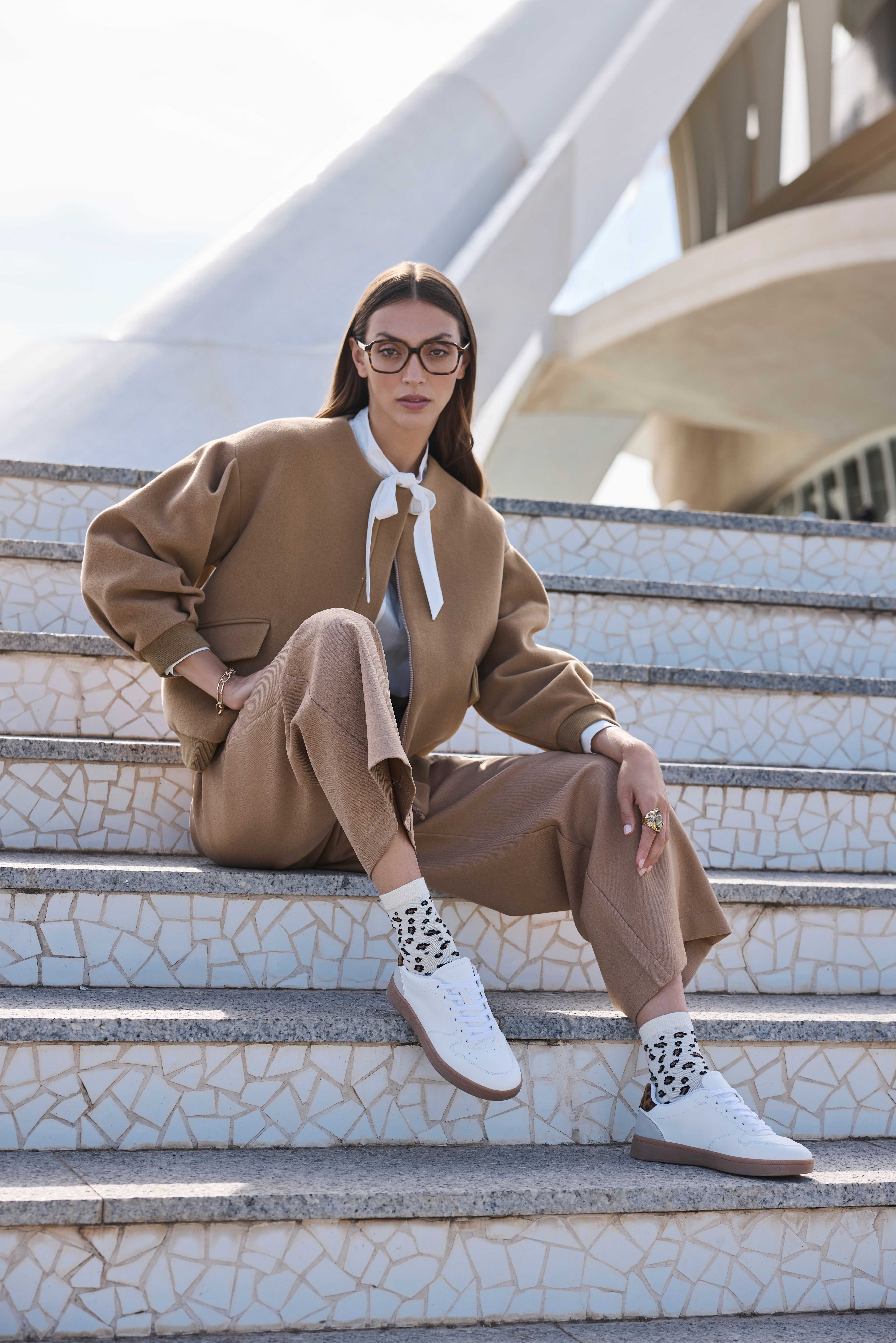 Eine Frau trägt ein beiges Anzug-Set mit weißer Bluse, dazu gemusterte Socken im Animal-Print und weiße Sneakers