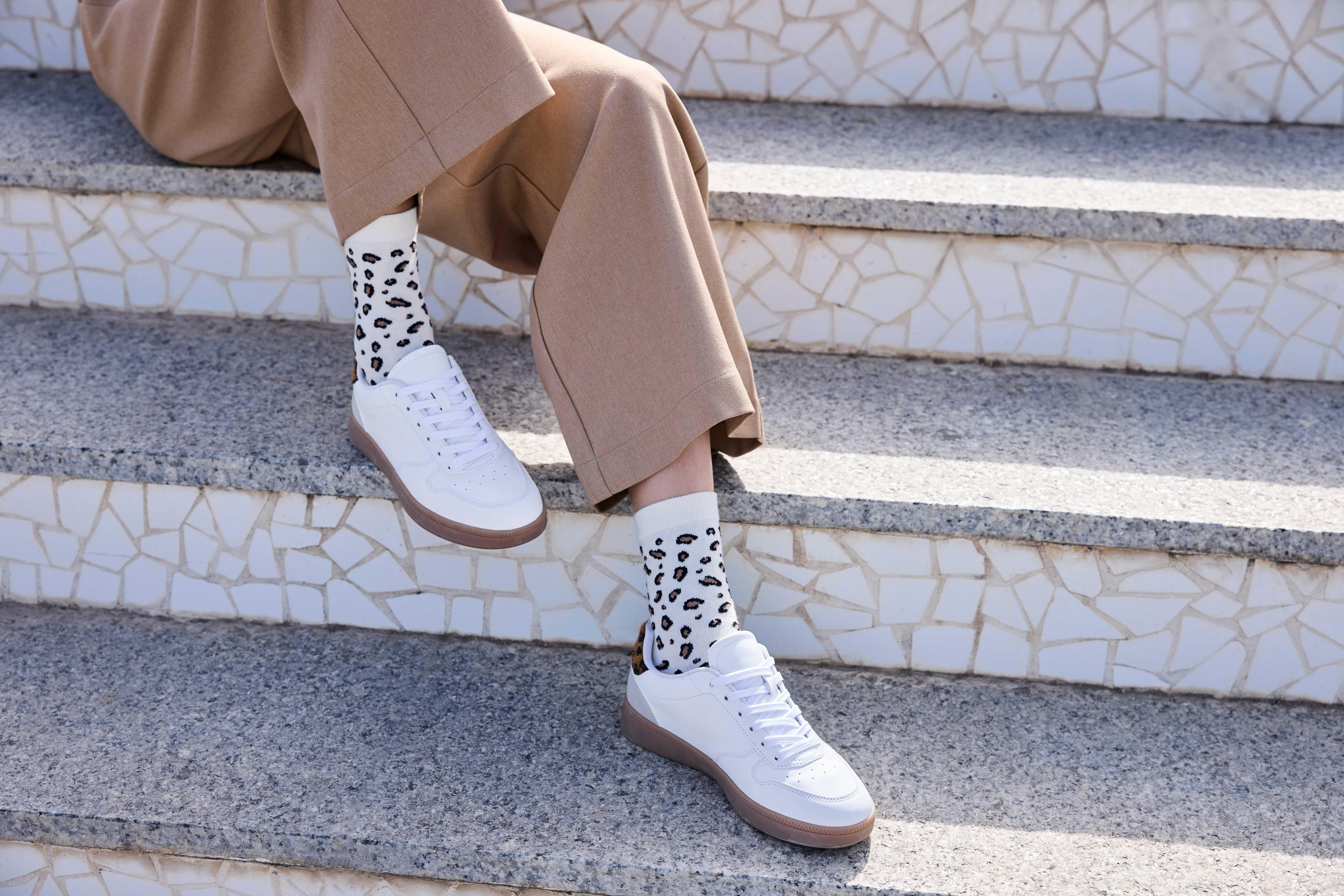 Eine Frau trägt beige weite Hosen, weiße Sneaker und gemusterte Socken mit Animal-Print