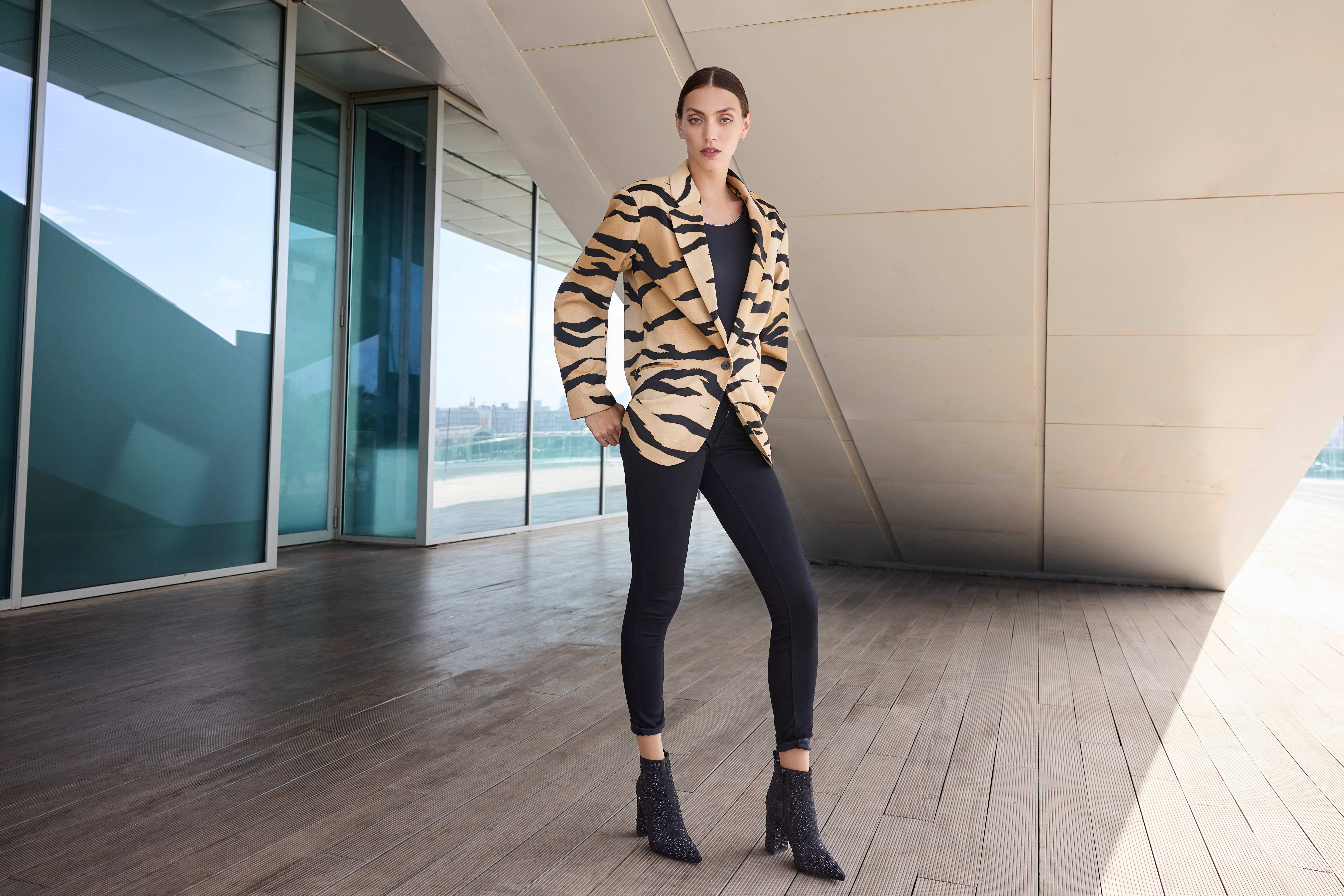 Eine Frau trägt eine schwarze Hose mit schwarzem Top und einem auffälligen Blazer im Tigerstreifen-Muster