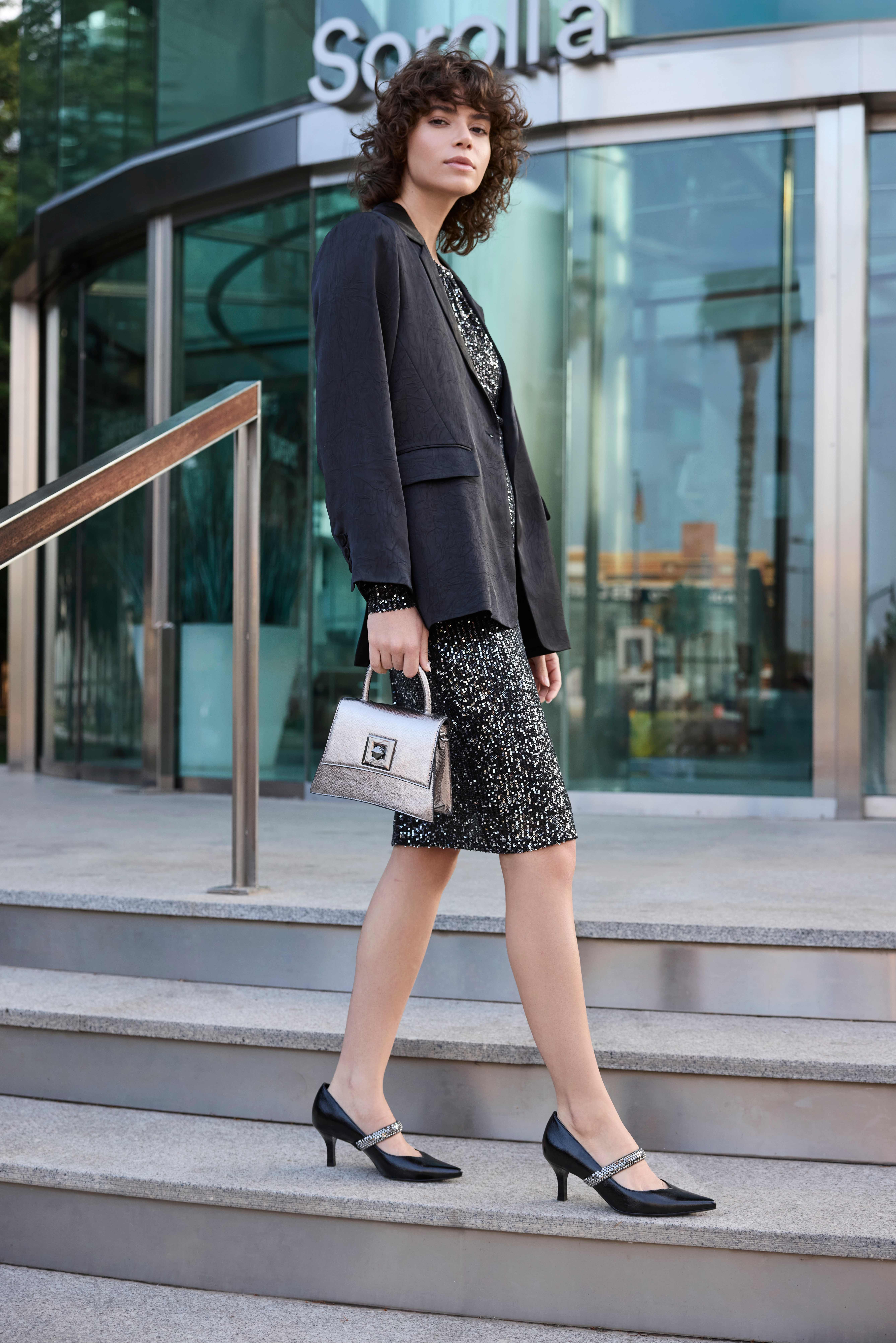 Frau in schwarzem Blazer mit Glitzer-Dress, kombiniert mit silberner Handtasche
