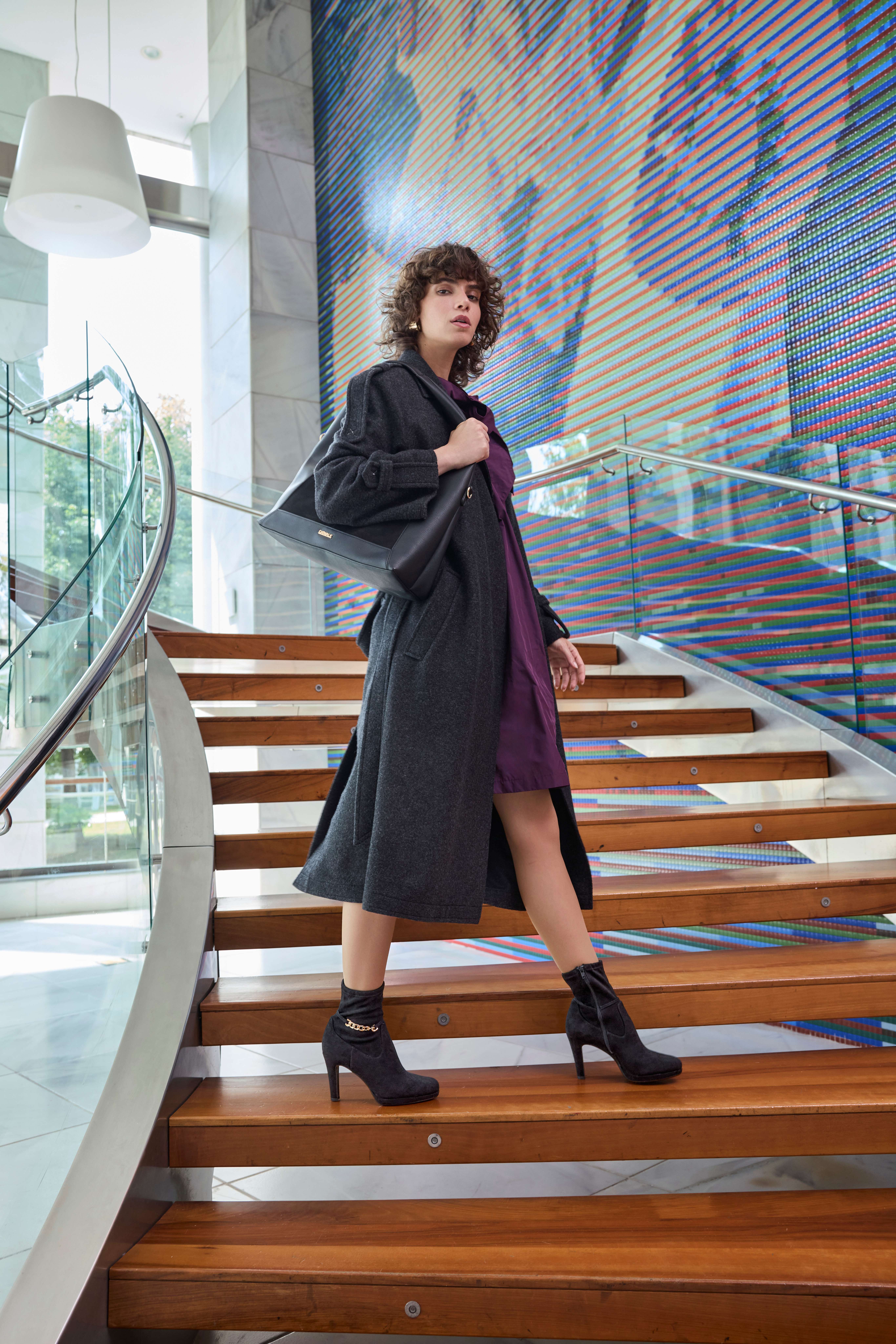 Frau in schwarzem Mantel und auberginefarbenem Kleid, mit schwarzen Heels, stehend auf Treppe