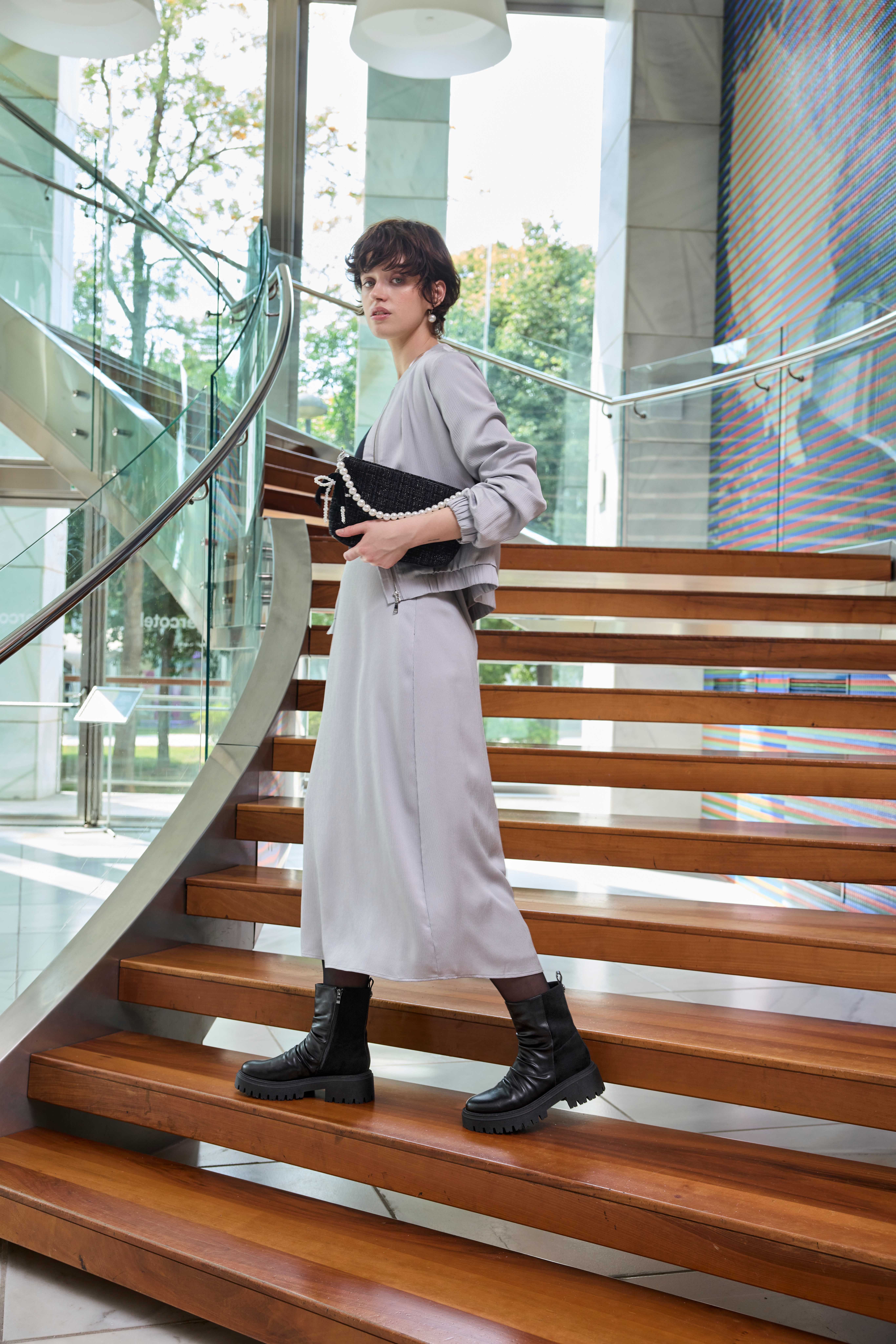 Frau in weißem Kleid, trägt längliche Handtasche unterm Arm, steht auf Holztreppe