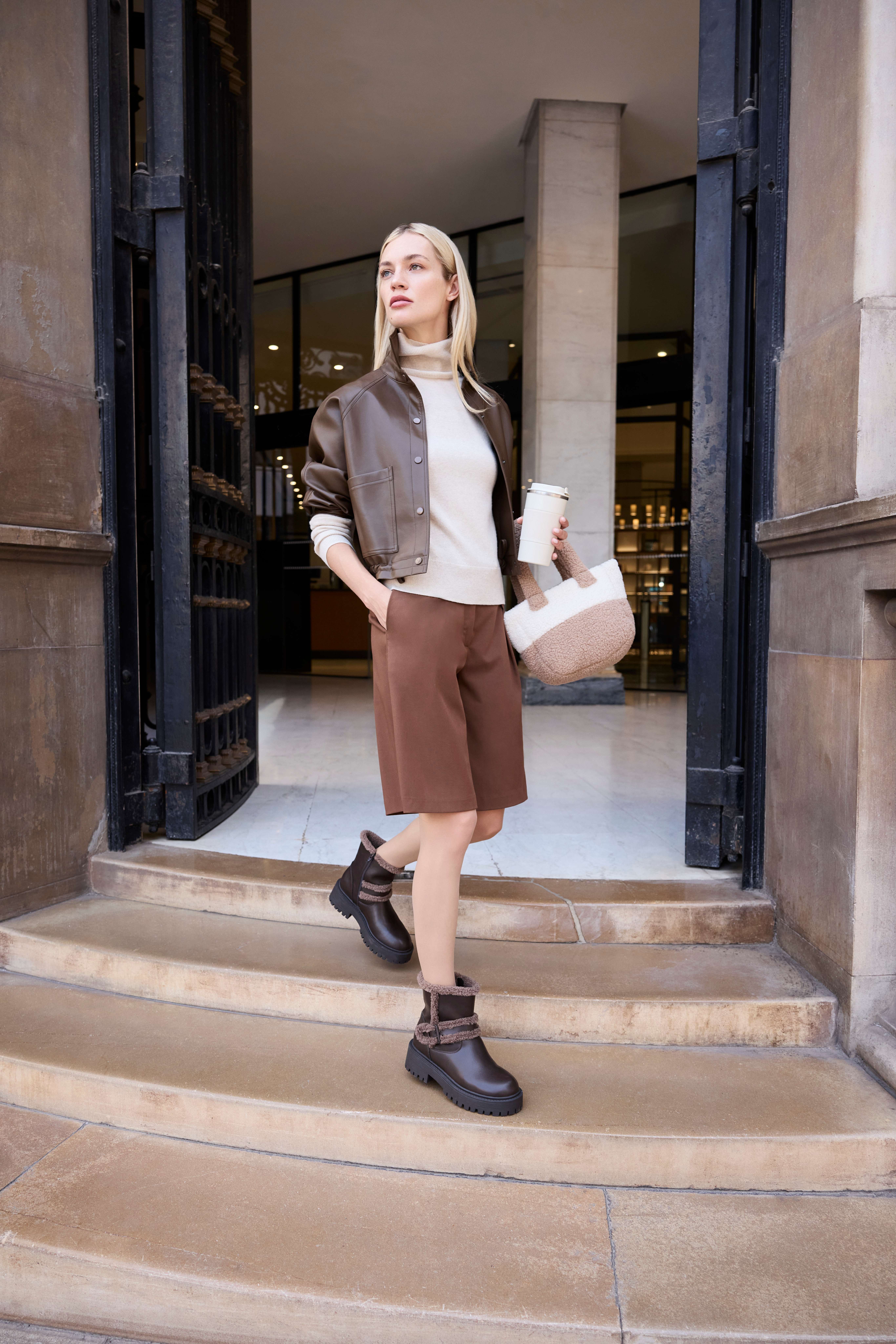 Frau trägt Kombination aus kurzem Blouson, Turtle Neck und Bermudas mit Chunky Boots