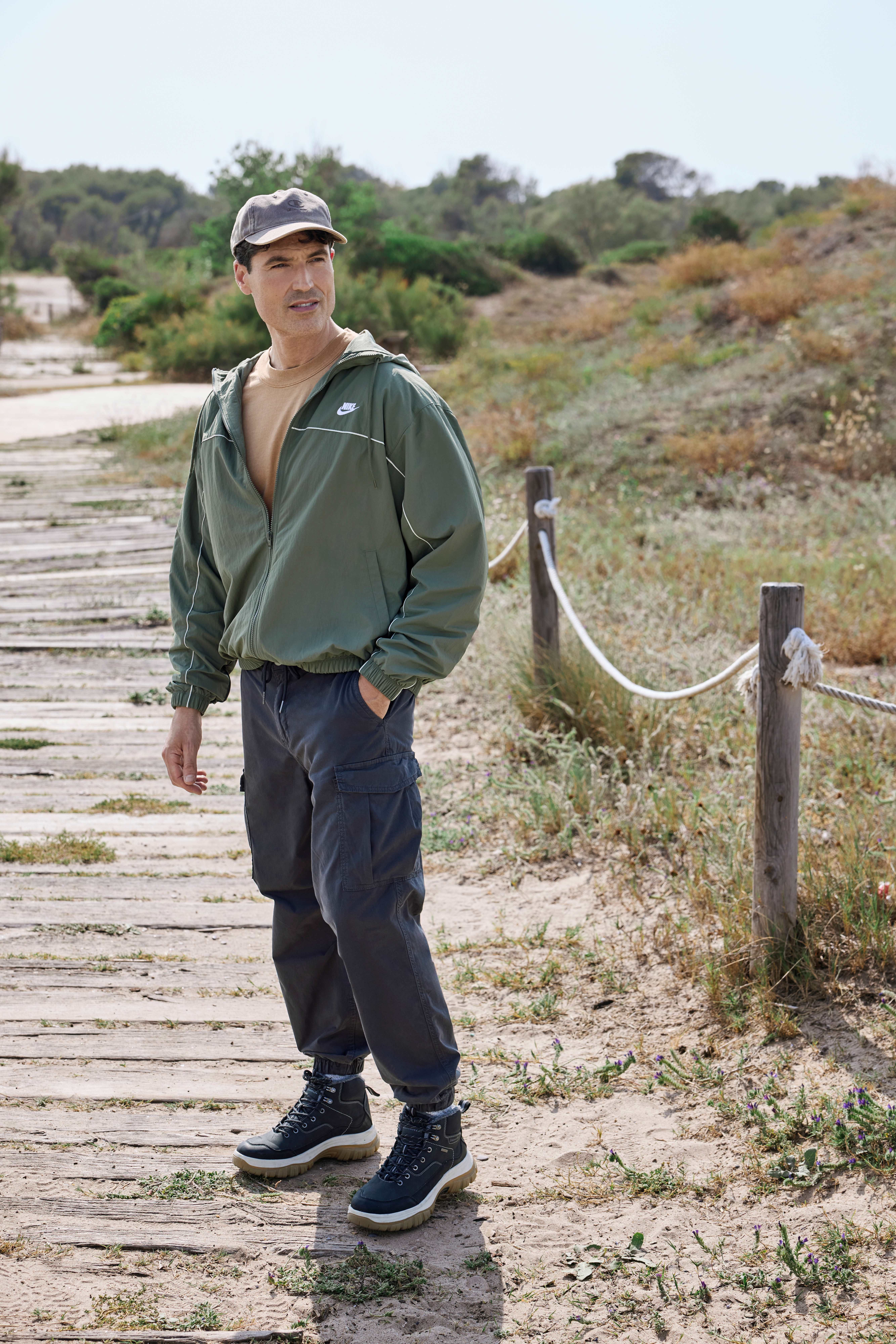 Mann mit dunkelgrüner Windjacke, schwarzen Cargopants und passenden Outdoor-Sneakern