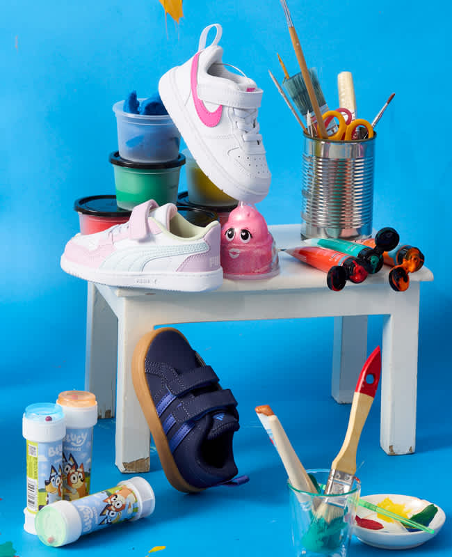 Herbsttaugliche Sneaker für Kinder auf einem Tisch, umgeben von bunten Mal- und Bastelutensilien, vor blauem Hintergrund.