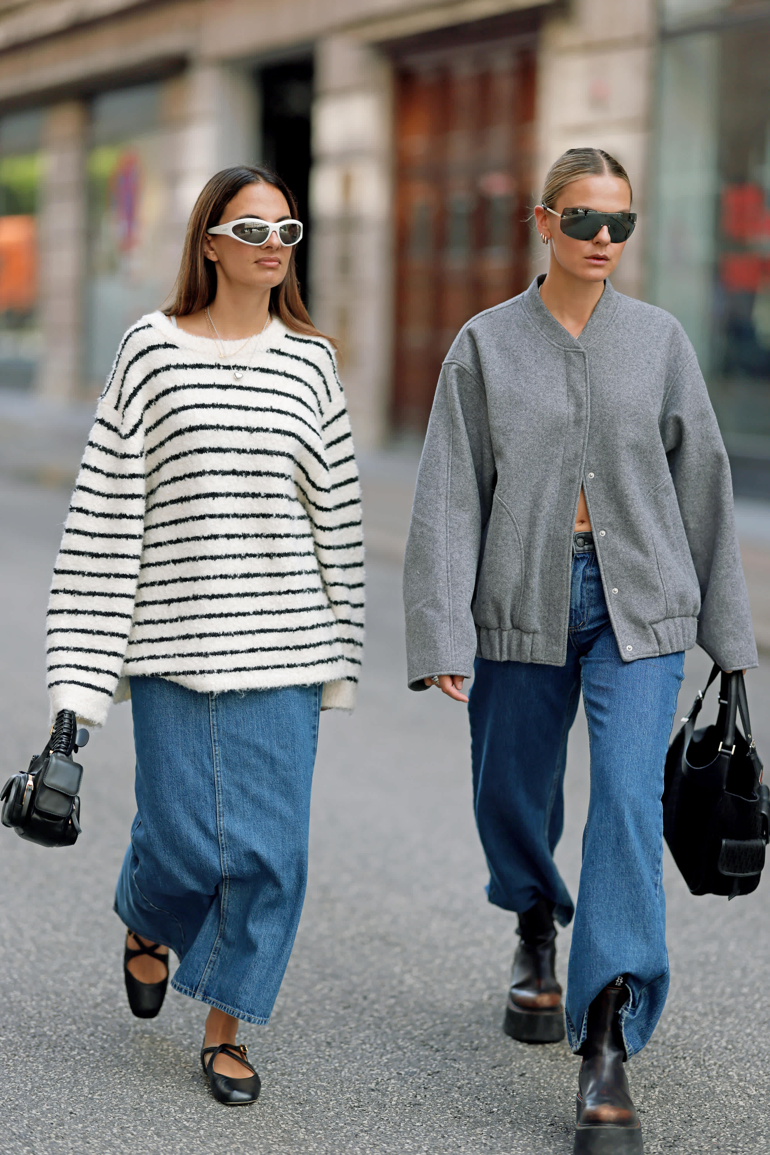 Zwei Frauen in lässiger Oversized-Streetwear, links mit gestreiftem Oversize-Pullover und Jeansrock, rechts mit grauer Jacke, weiter Jeans und schwarzen Stiefeln